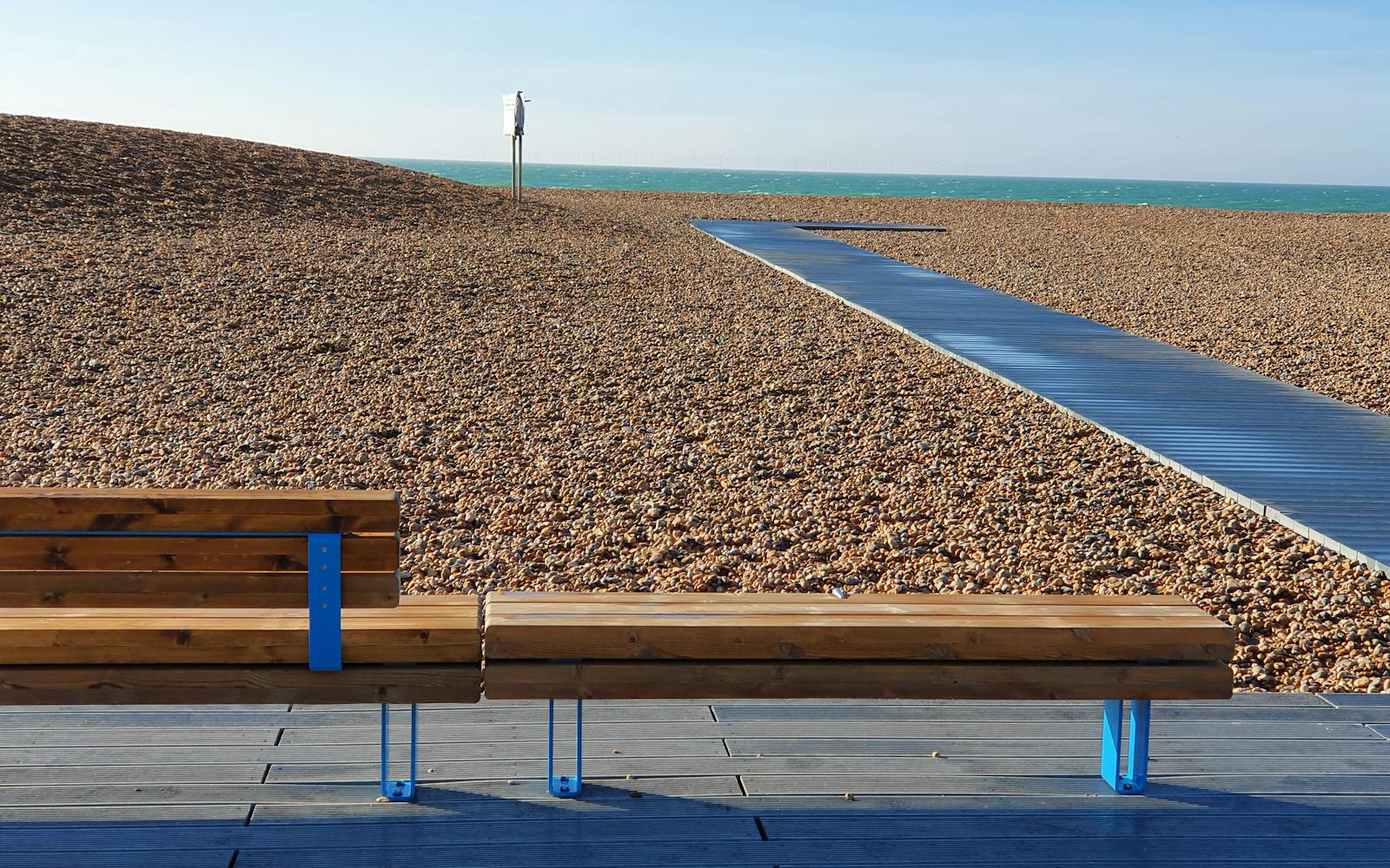 A wooden bench on a boardwalk overlooks a pebble beach and the sea.