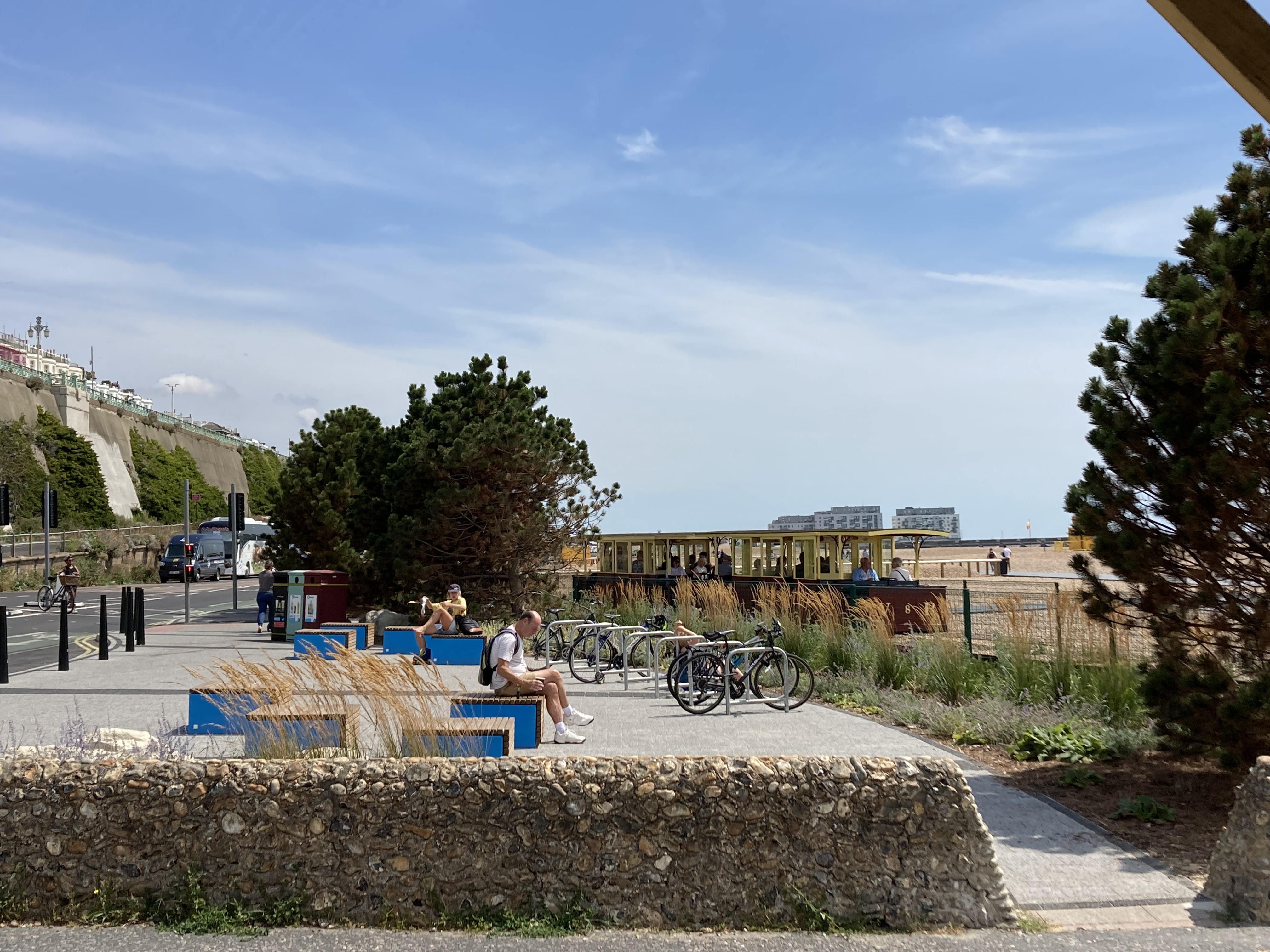A paved area with benches and bicycles, with a beach and sea in the background.