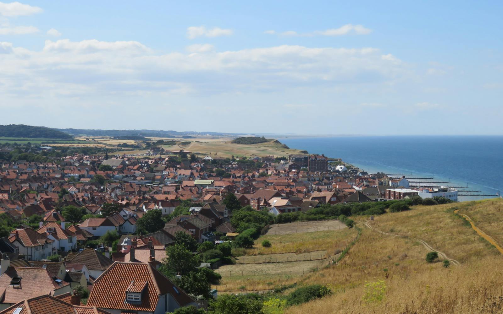 A high-angle view of a coastal town with red-tiled roofs, stretching towards a blue sea on a sunny day.