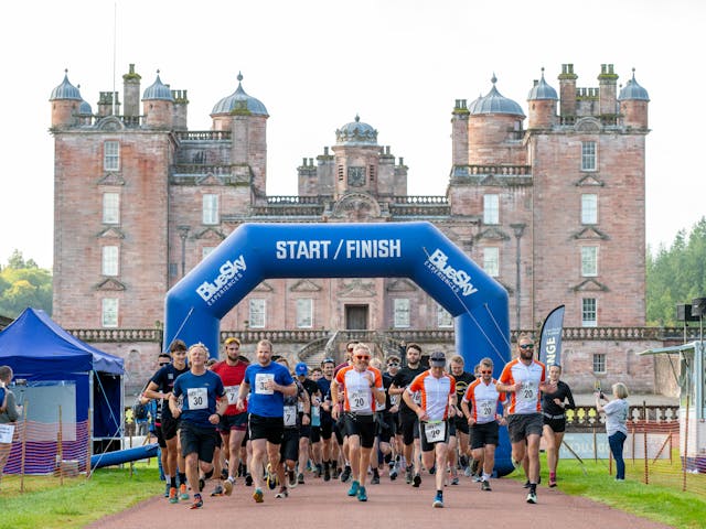 A group of people in sport gear at the start of a race with a castle in the background