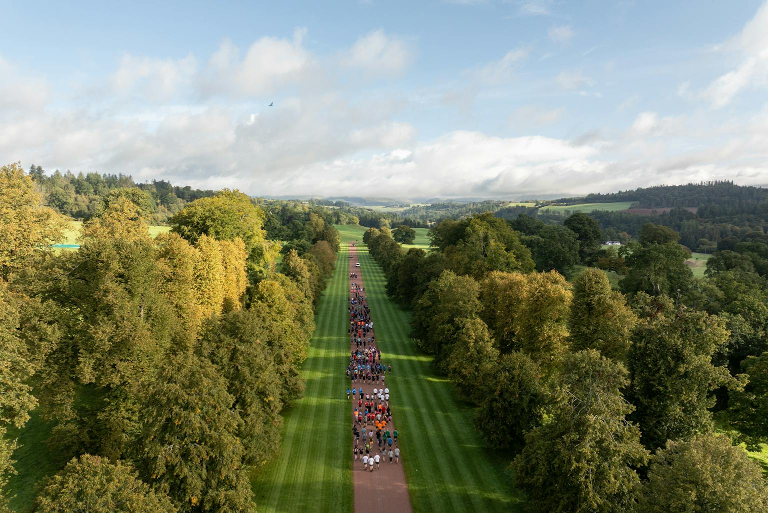 A drone photo showing a big group of people running on a path surrounded by green treas and grass.