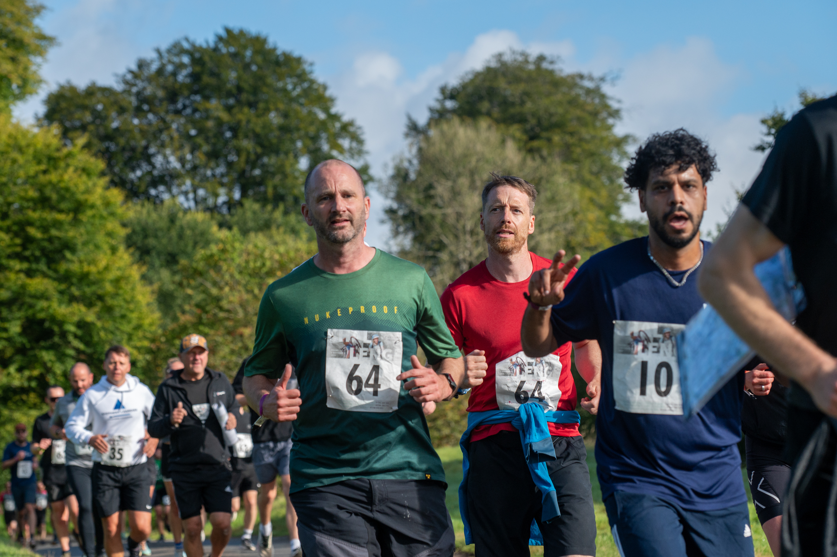 A group of people in sports gear racing in a leafy park.