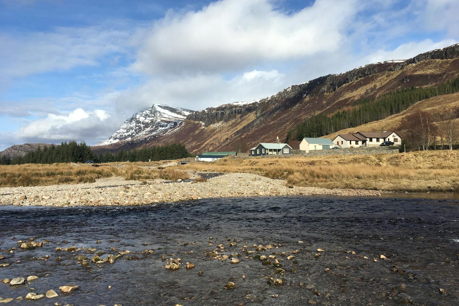 A Scottish landscape with snowy mountains and houses on the shore of a loch