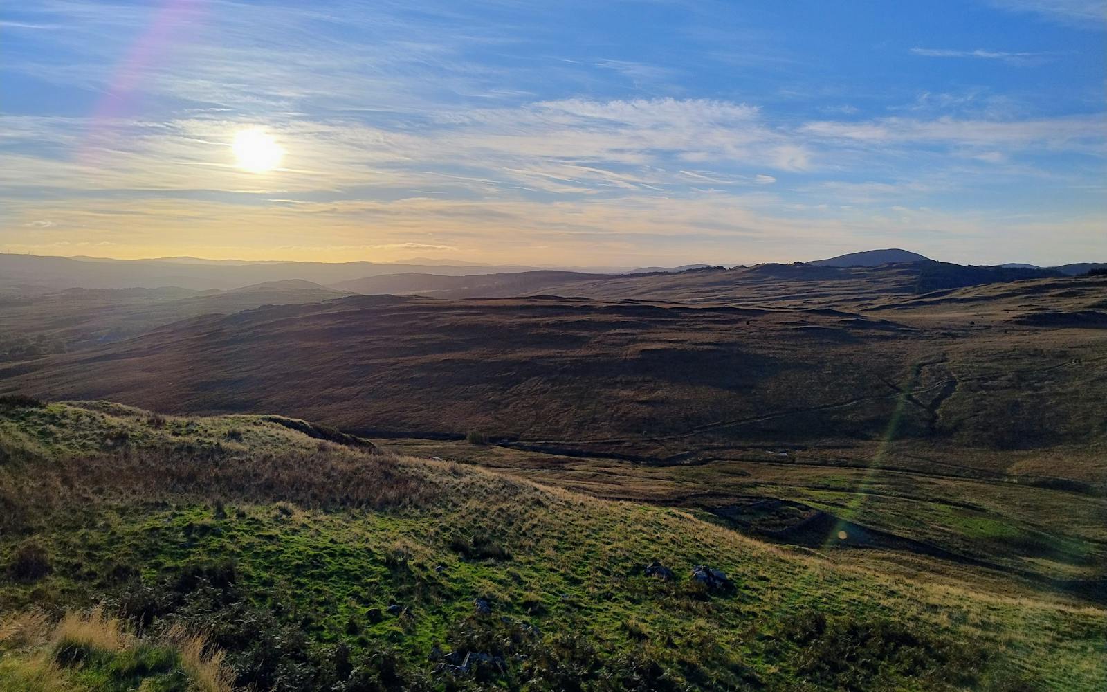 A Scottish landscape with mountains and moors with a hazy sun in blue skies