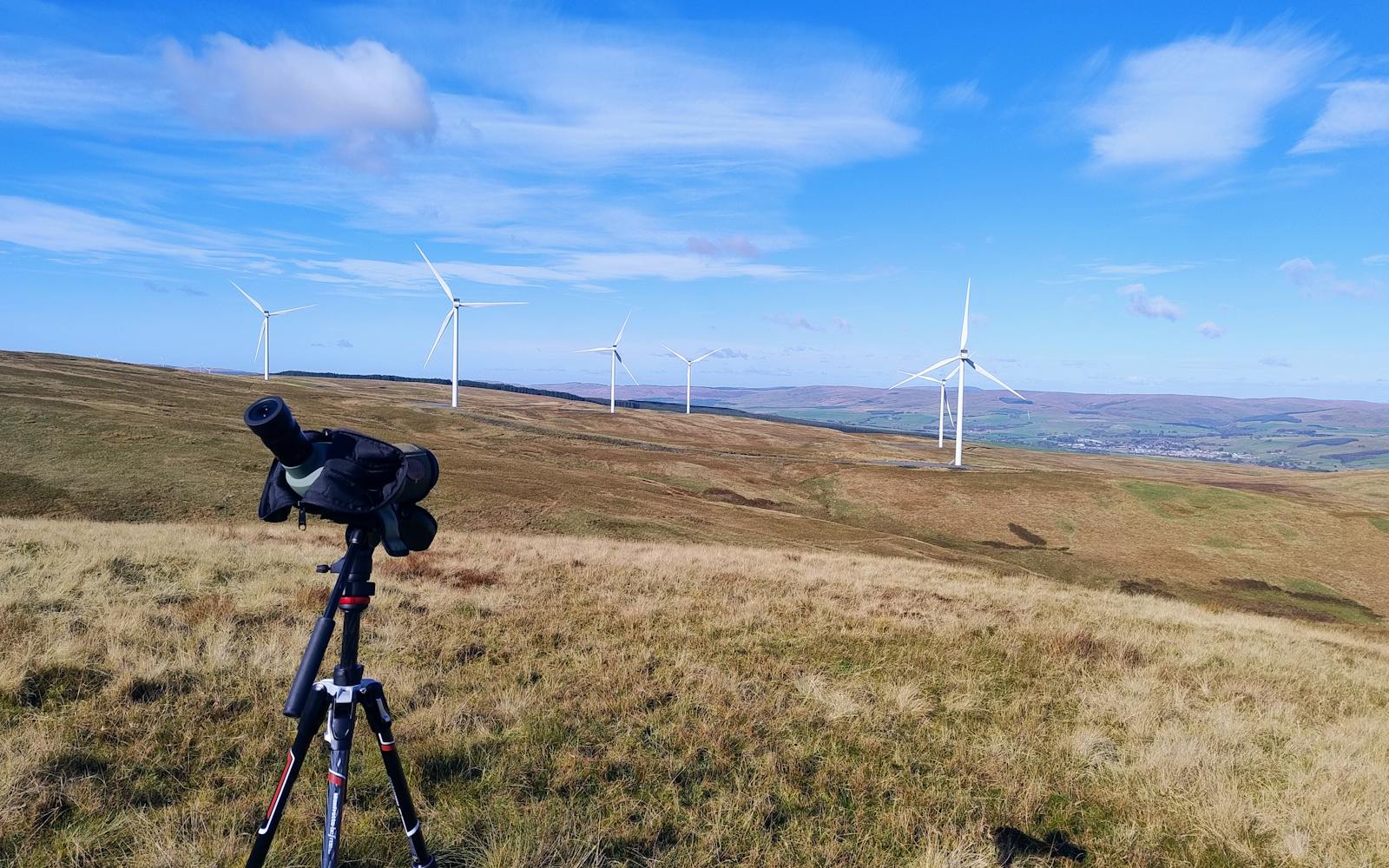 A Scottish landscape with hills and moors with wind turbines in the background and a camera on a tripod in the foreground