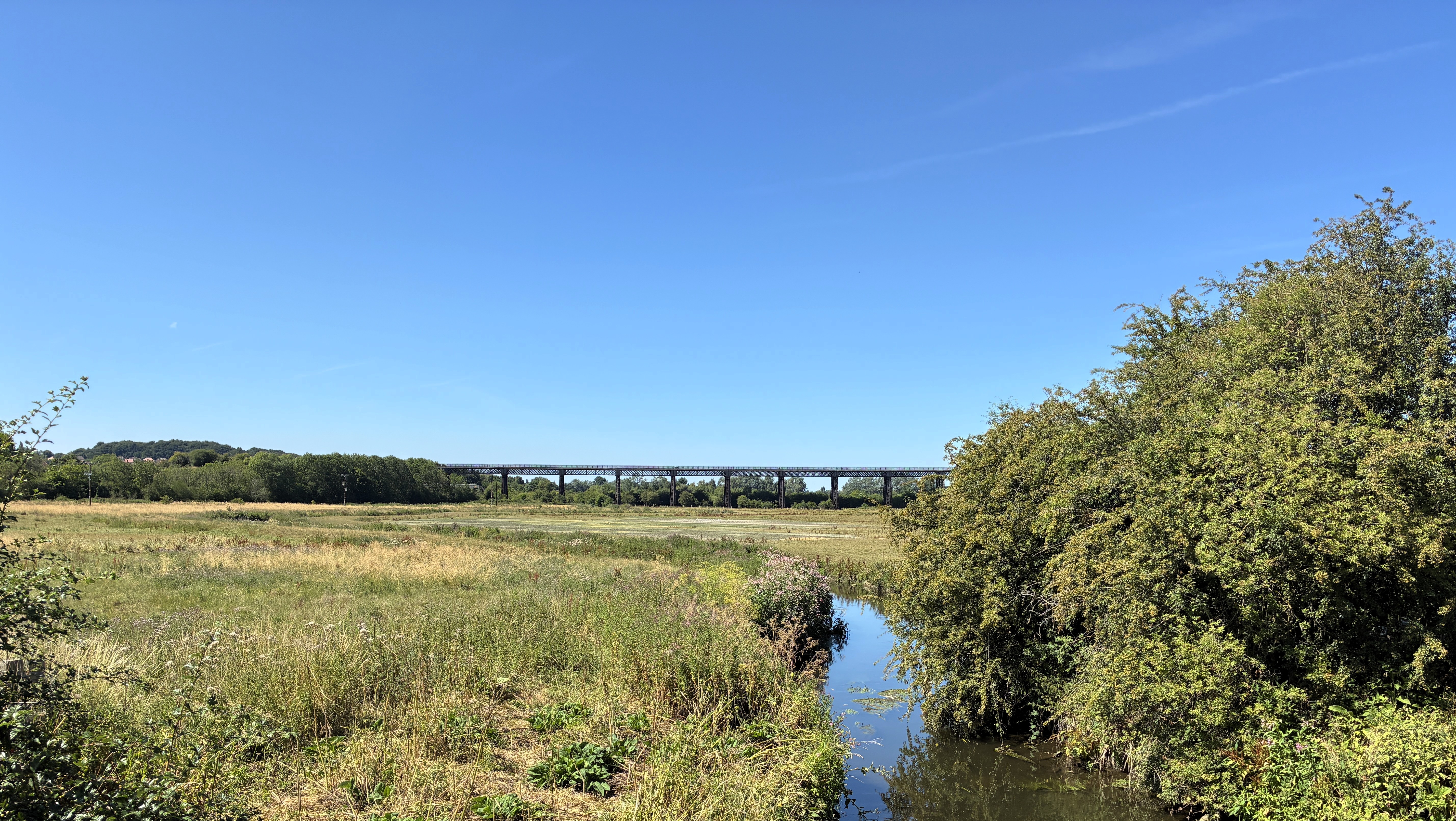 A river with fields and trees with a bridge in the background