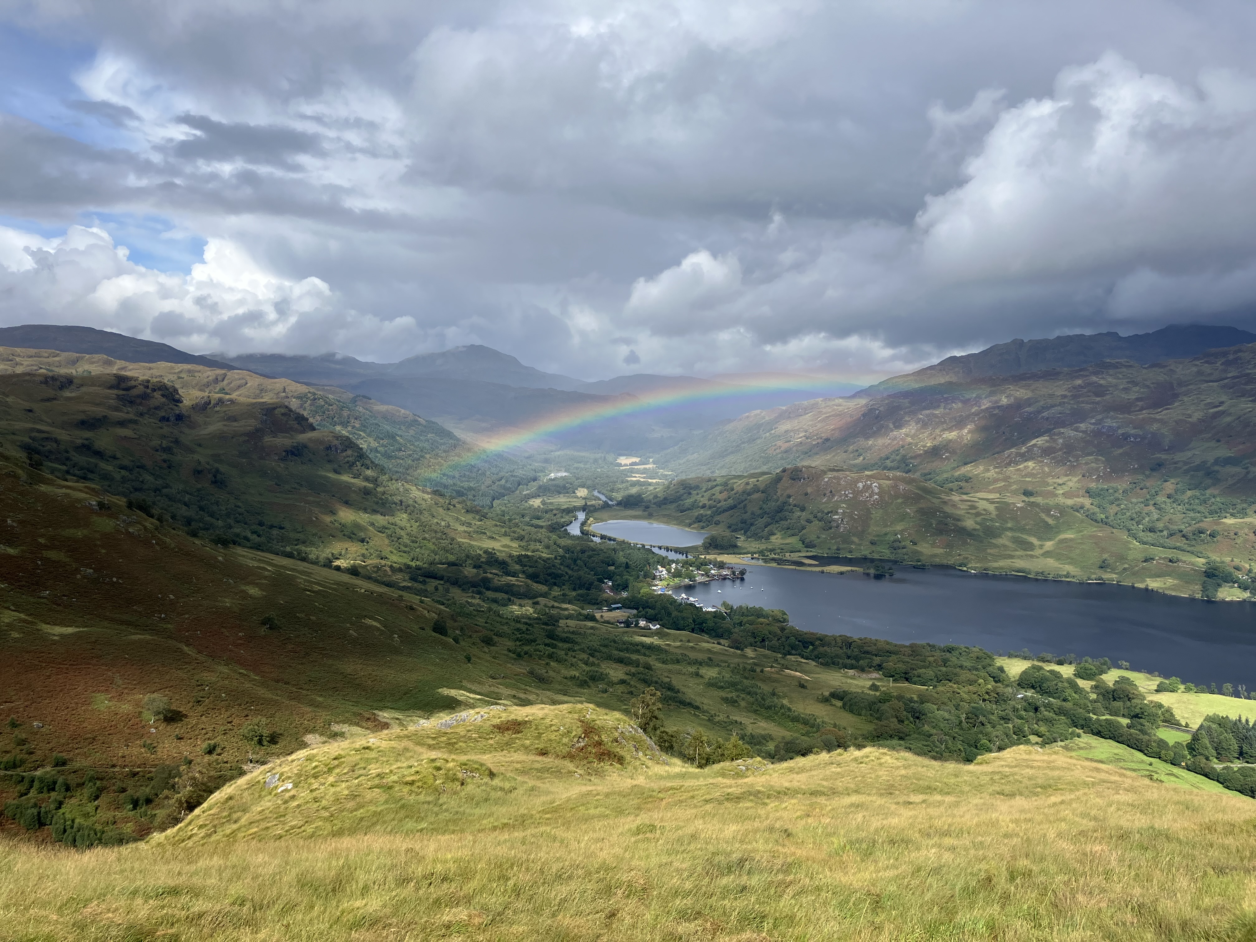 A view over Scottish mountains and Loch Lomond with a rainbow in the background