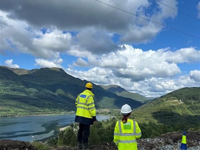 Two people in high-vis looking out over hills and a lake