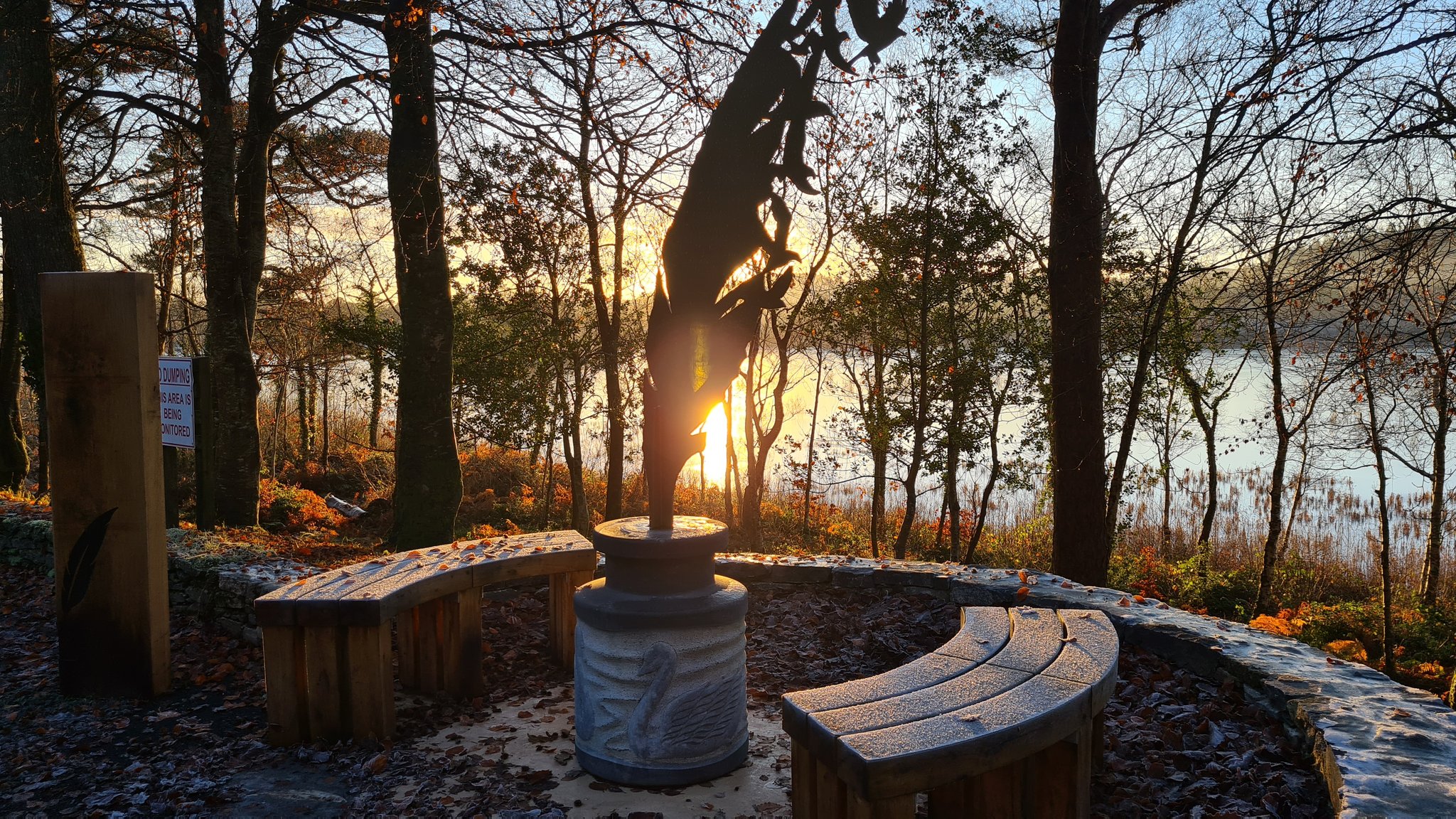 A bench and street furniture overlooking water and a sunset