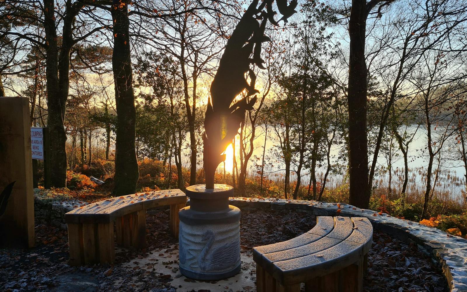 A bench and street furniture overlooking water and a sunset