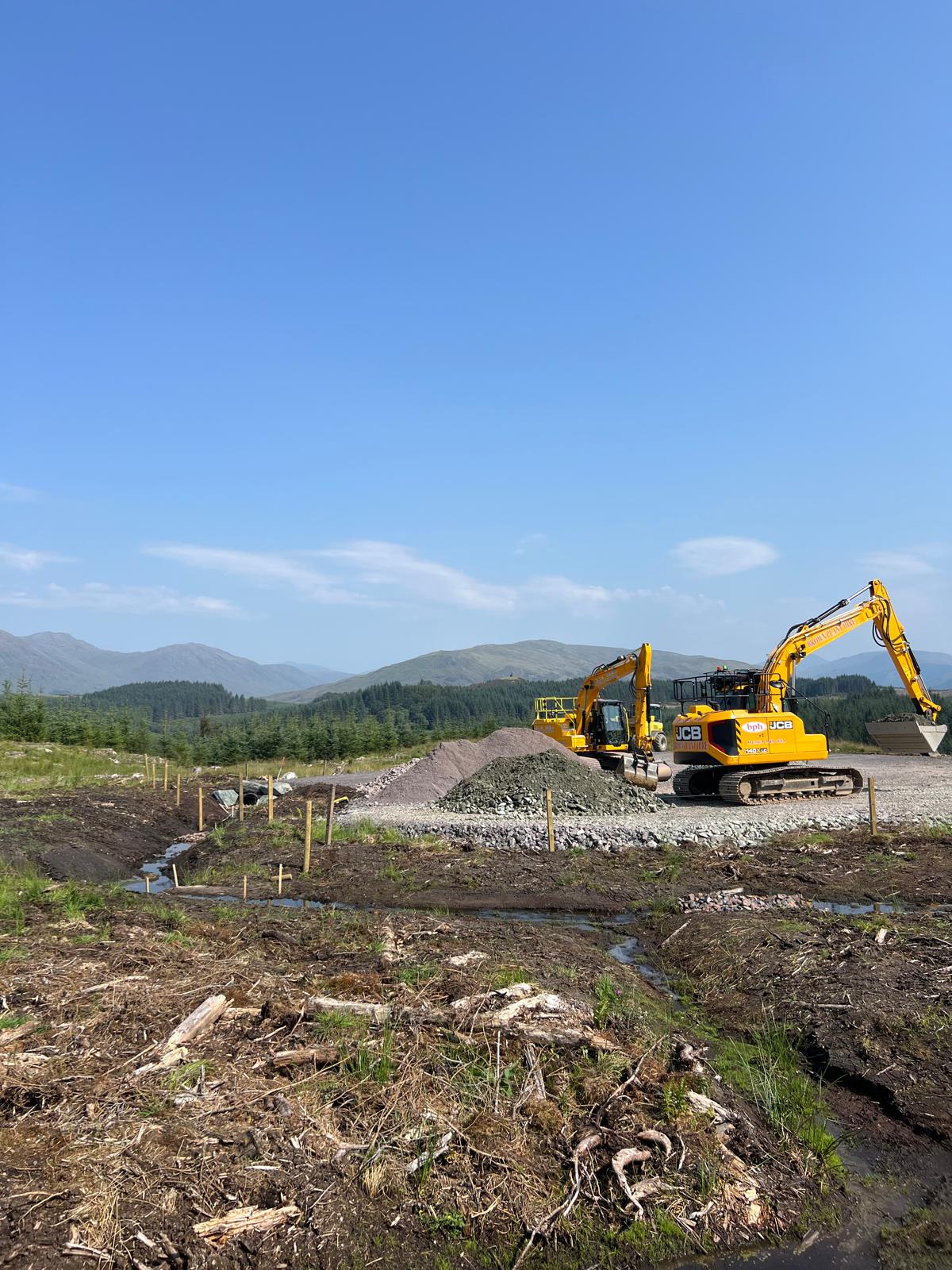 A digger moving stones with hills in the background under a blue sky.