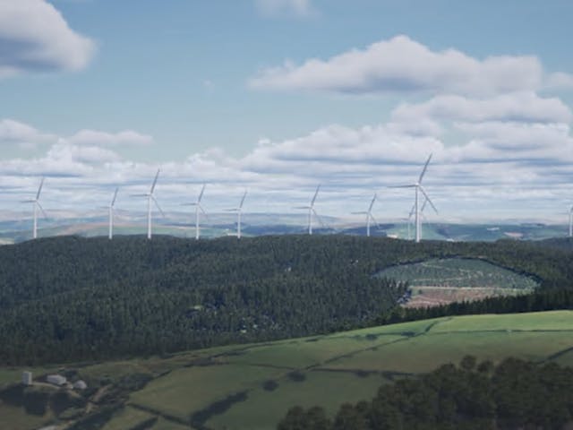 A row of white wind turbines stands along the crest of a densely forested hill, overlooking rolling green fields and valleys under a cloudy sky.