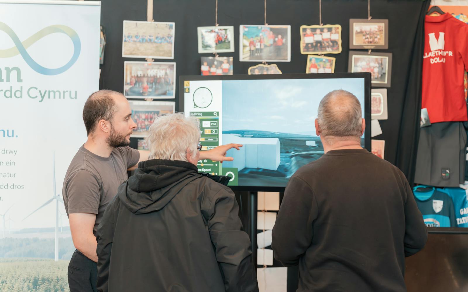Three people looking at a large screen displaying a digital architectural or landscape model at a community event.