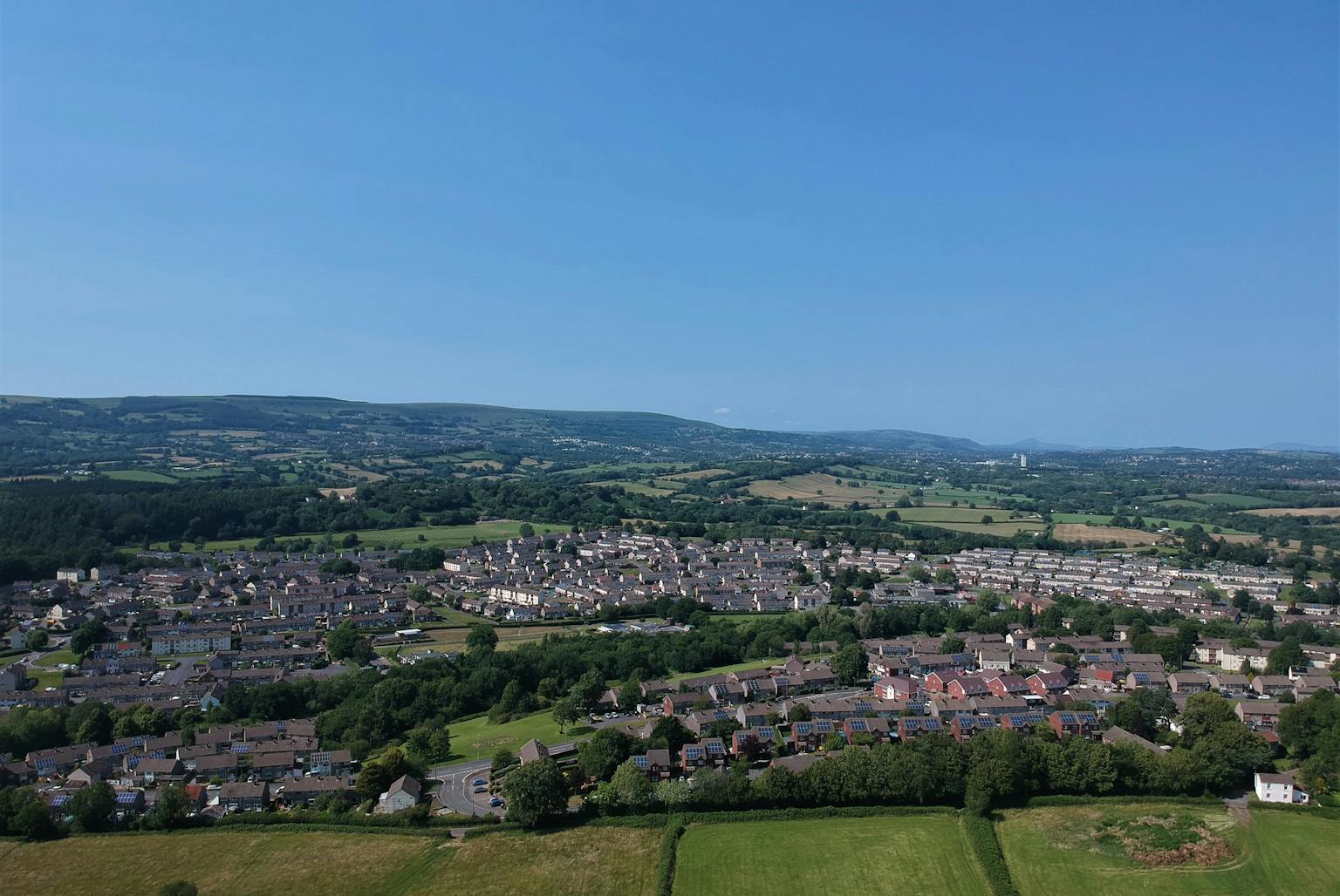 Aerial view of a town in Wales surrounded by green fields and blue sky