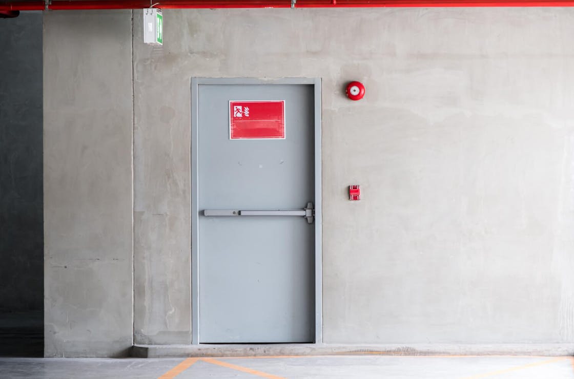 Fire door with panic hardware in a concrete wall, equipped with a seal and escape route signage – tested according to EN 16034 for preventive fire protection.