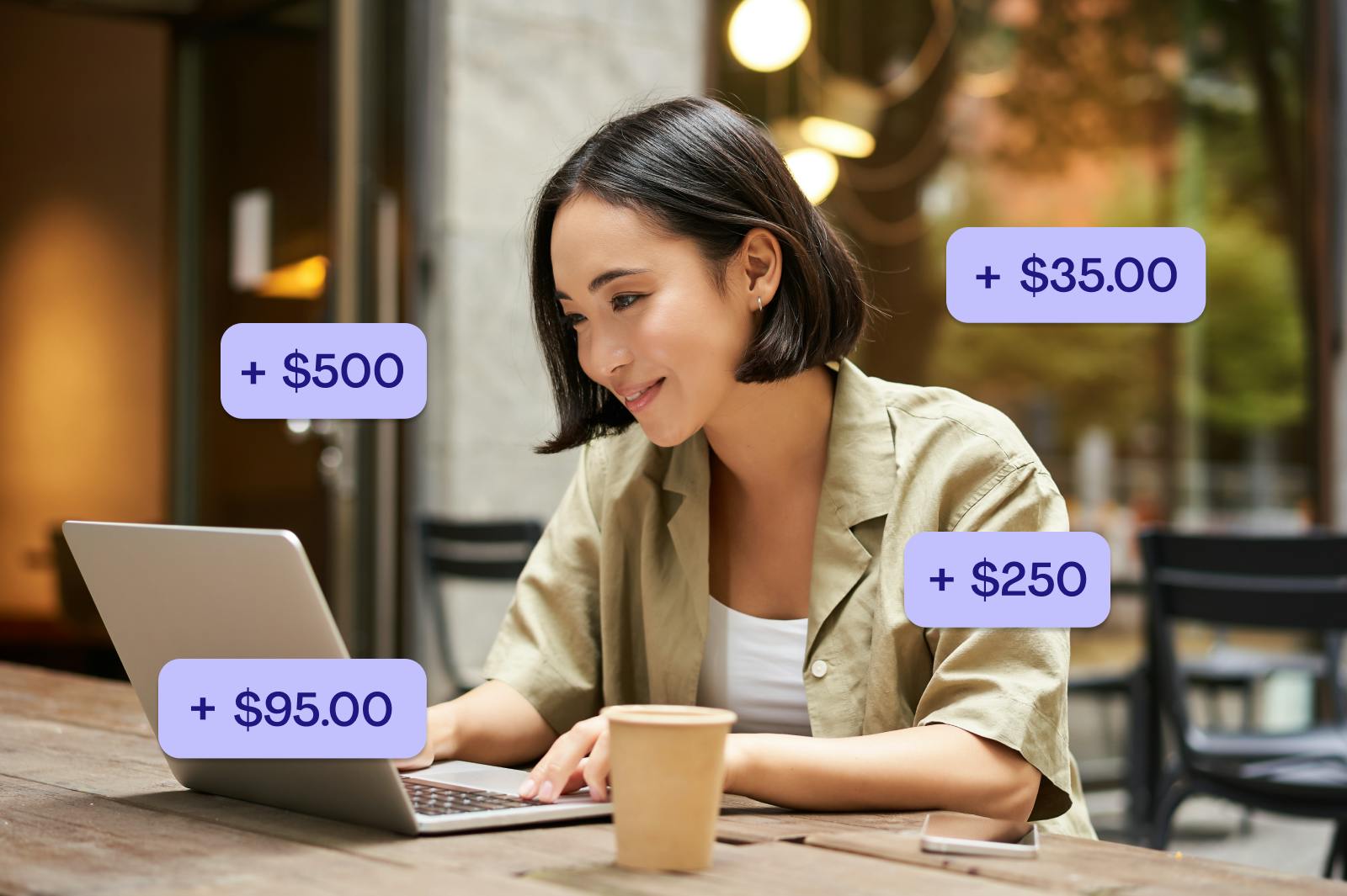a young asian woman smiles while working on her laptop at a cafe. little purple blocks with "+$500", "+$95", "+$250" and "+$35" float around her.