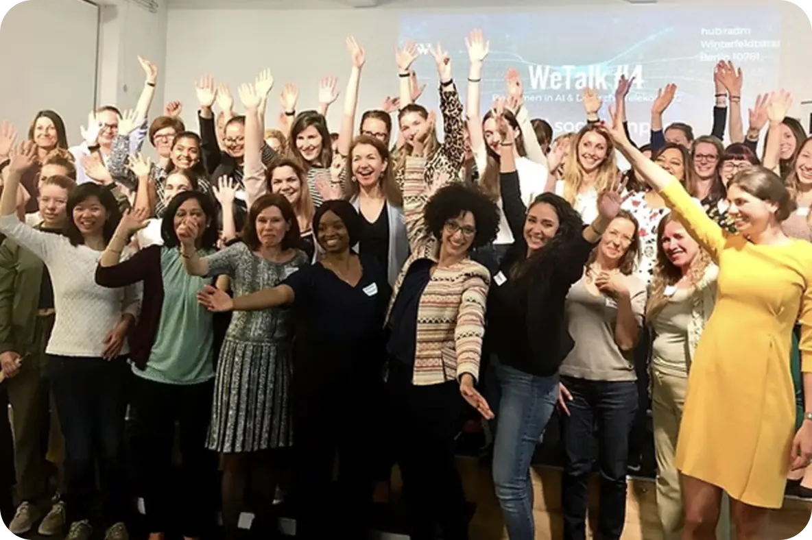 A large group of smiling people posing together with raised hands at an indoor event.