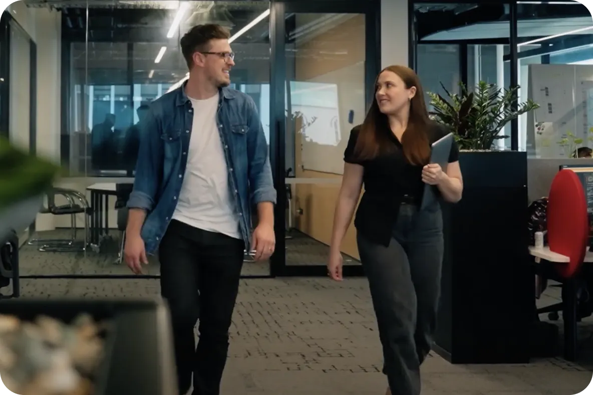 Two colleagues walking through a modern office corridor while talking and smiling.