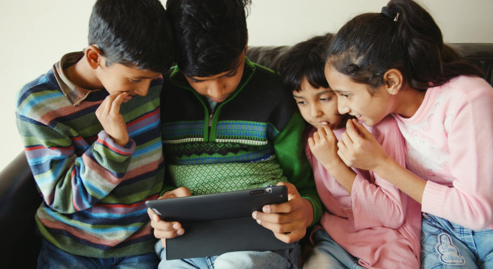 Four kids using an ipad on a couch