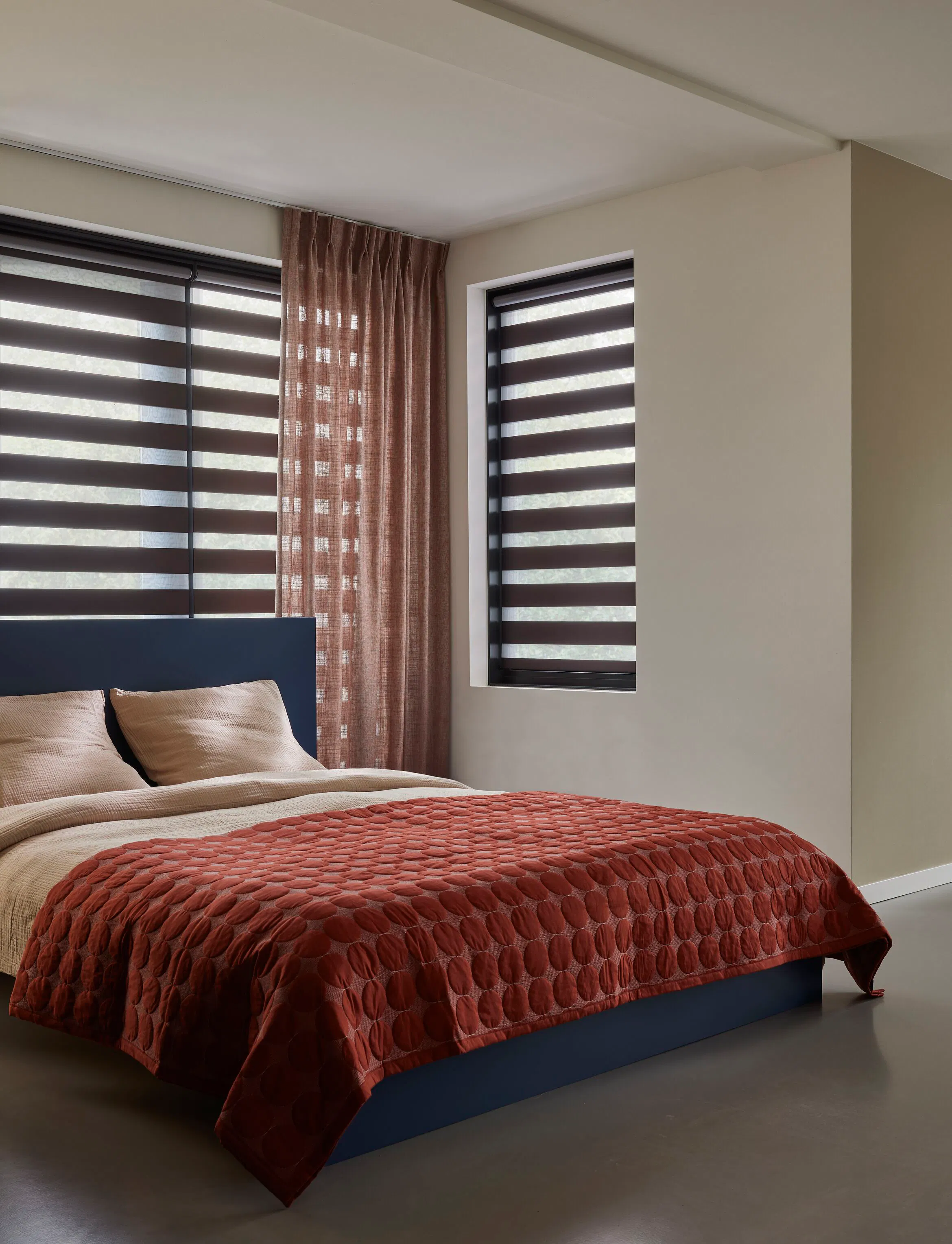 Brown duo roller blinds layered with sheer terracota curtains in a retro bedroom 