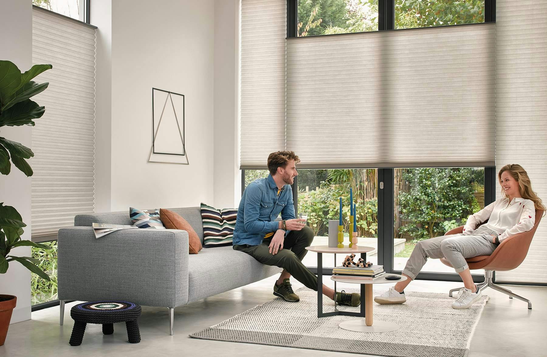 A man and a woman sitting in a living room with cream Duette® Shades on windows
