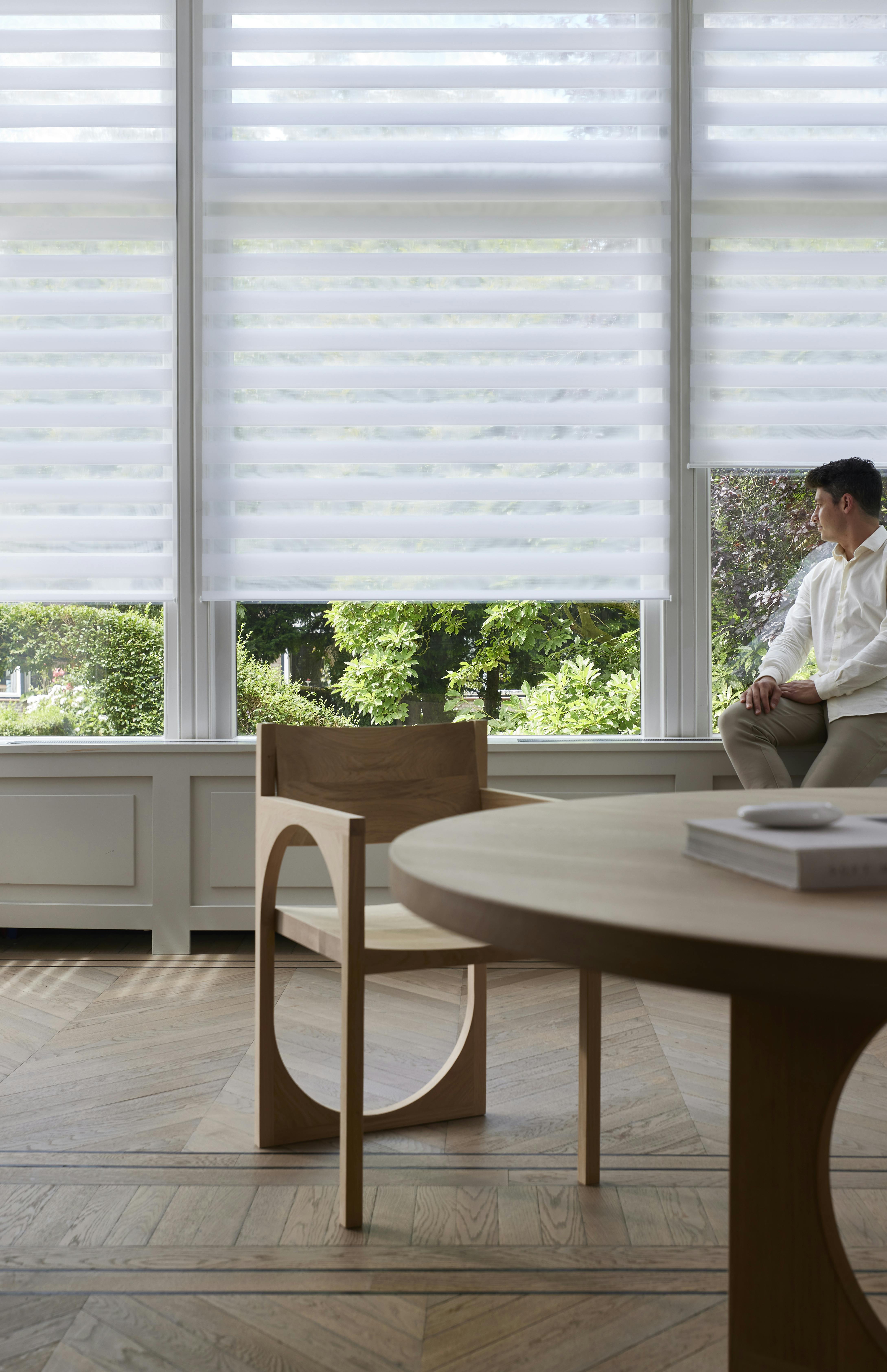 White duo roller blinds on a window and a man sitting on a window sill