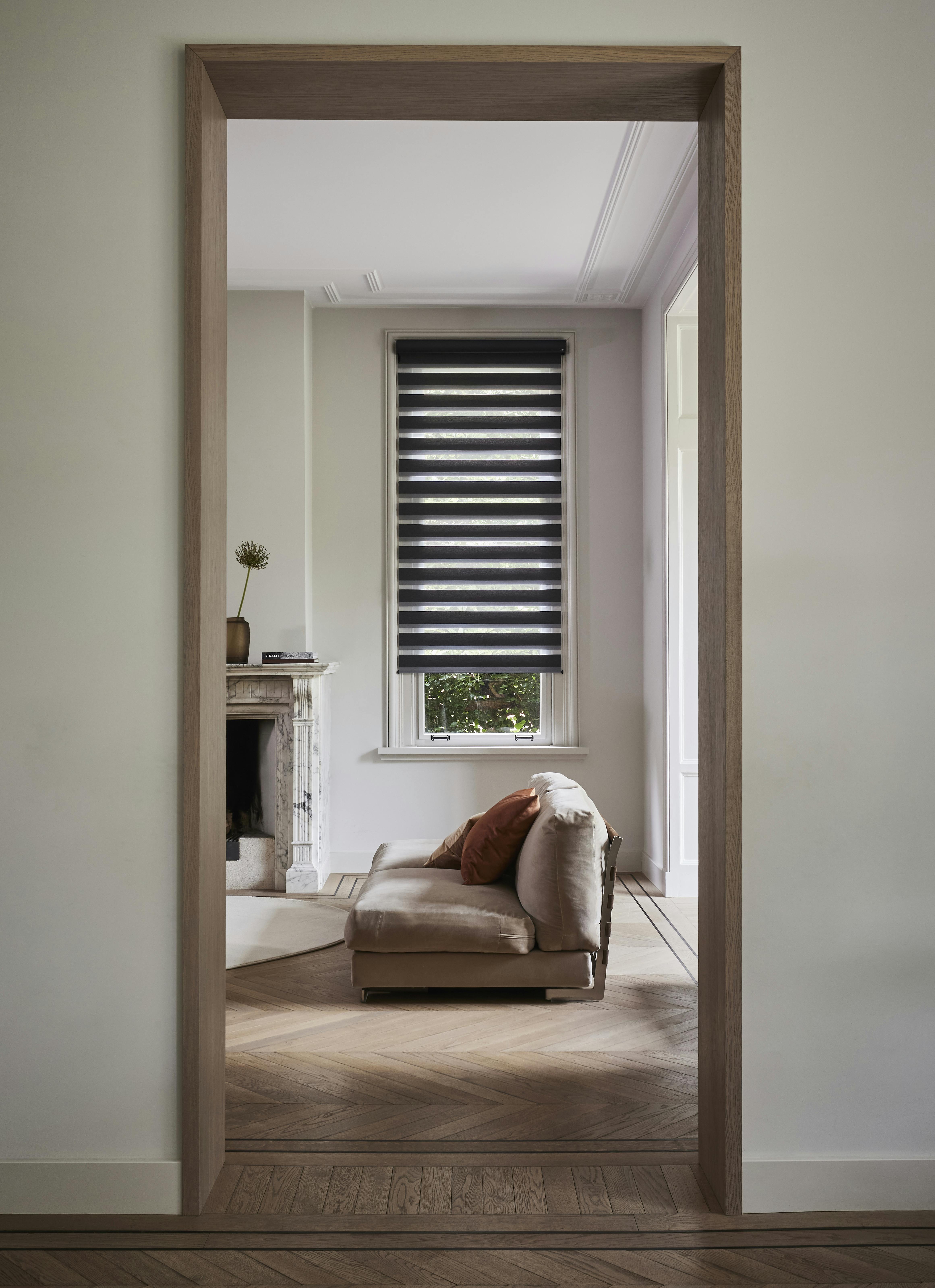 Brown duo roller blinds on a window in a living room seen from a distance 