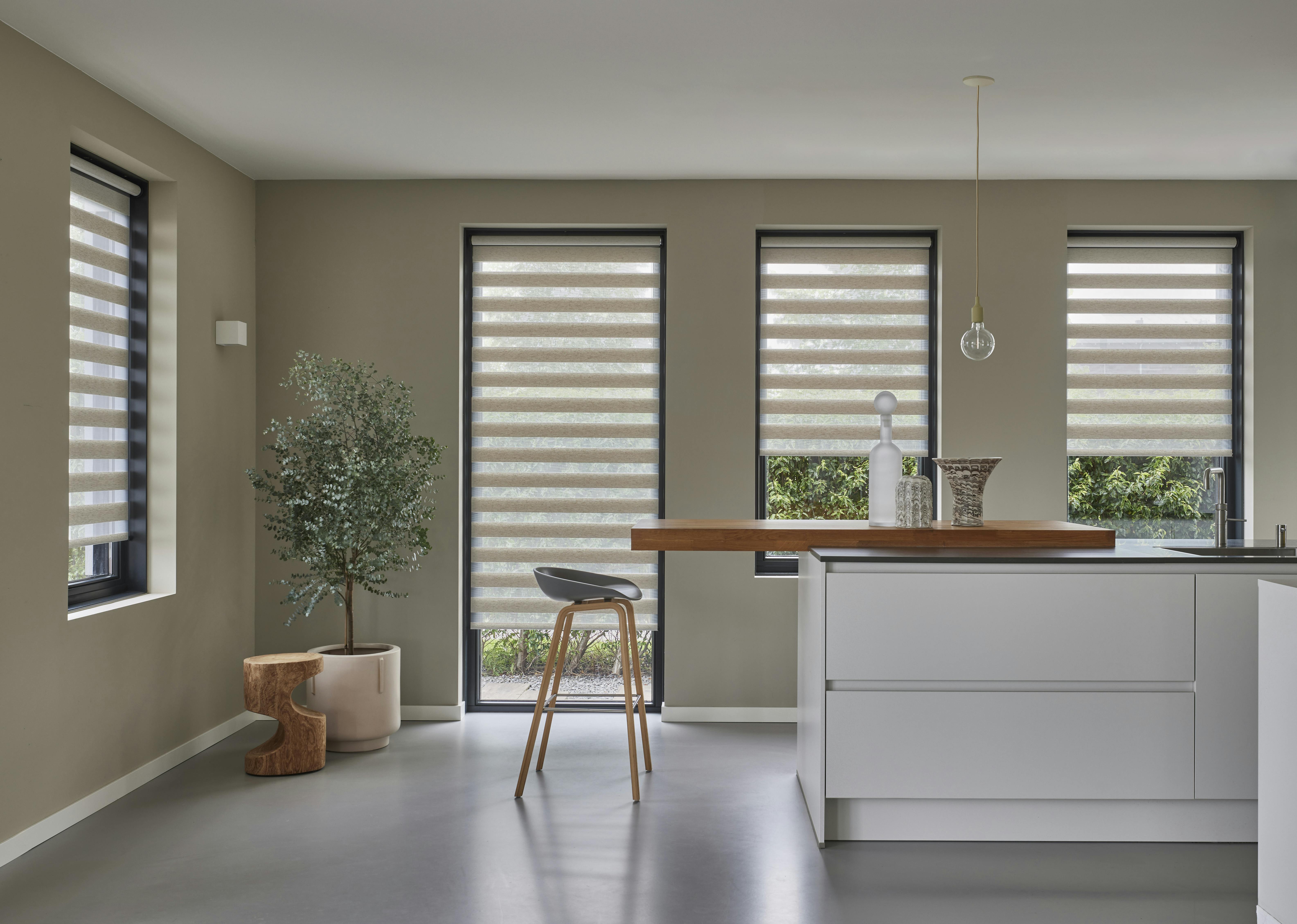 A spacious kitchen with cream duo roller blinds on large windows and a patio door 