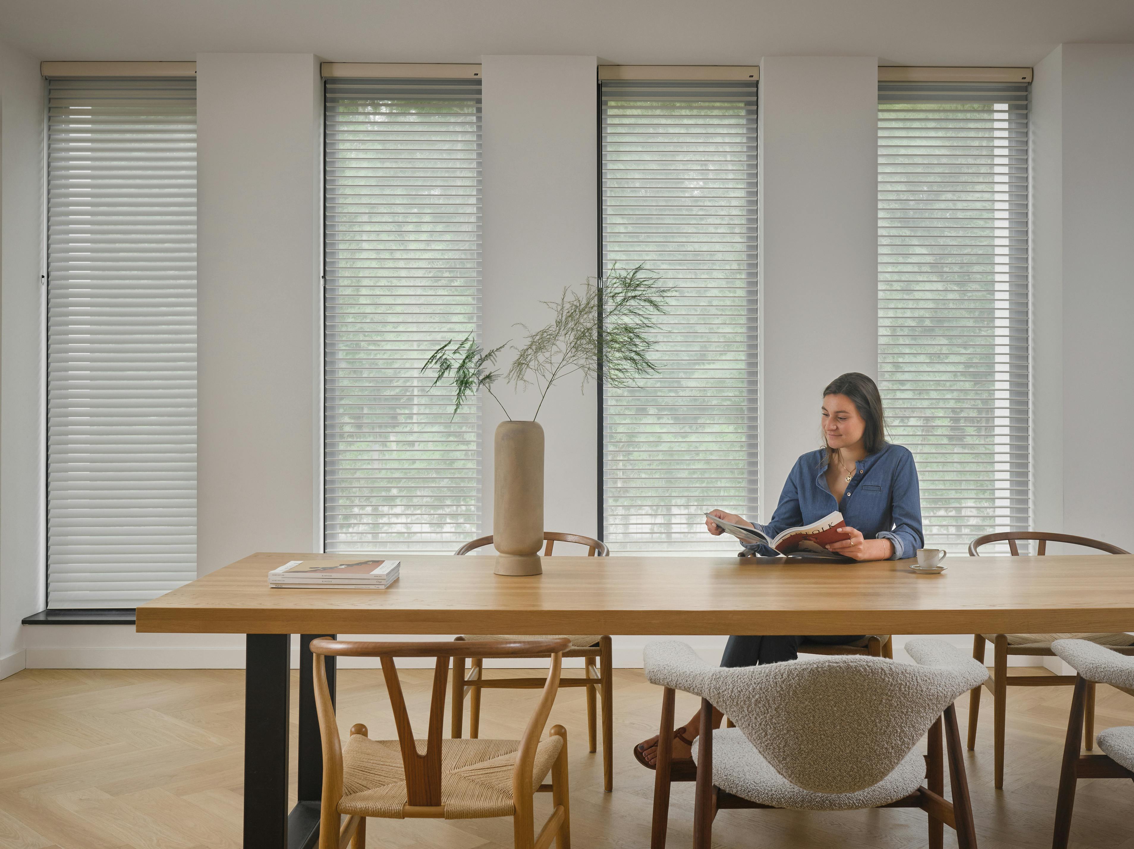 White silhouette shades on dining room windows with a woman reading a magazine