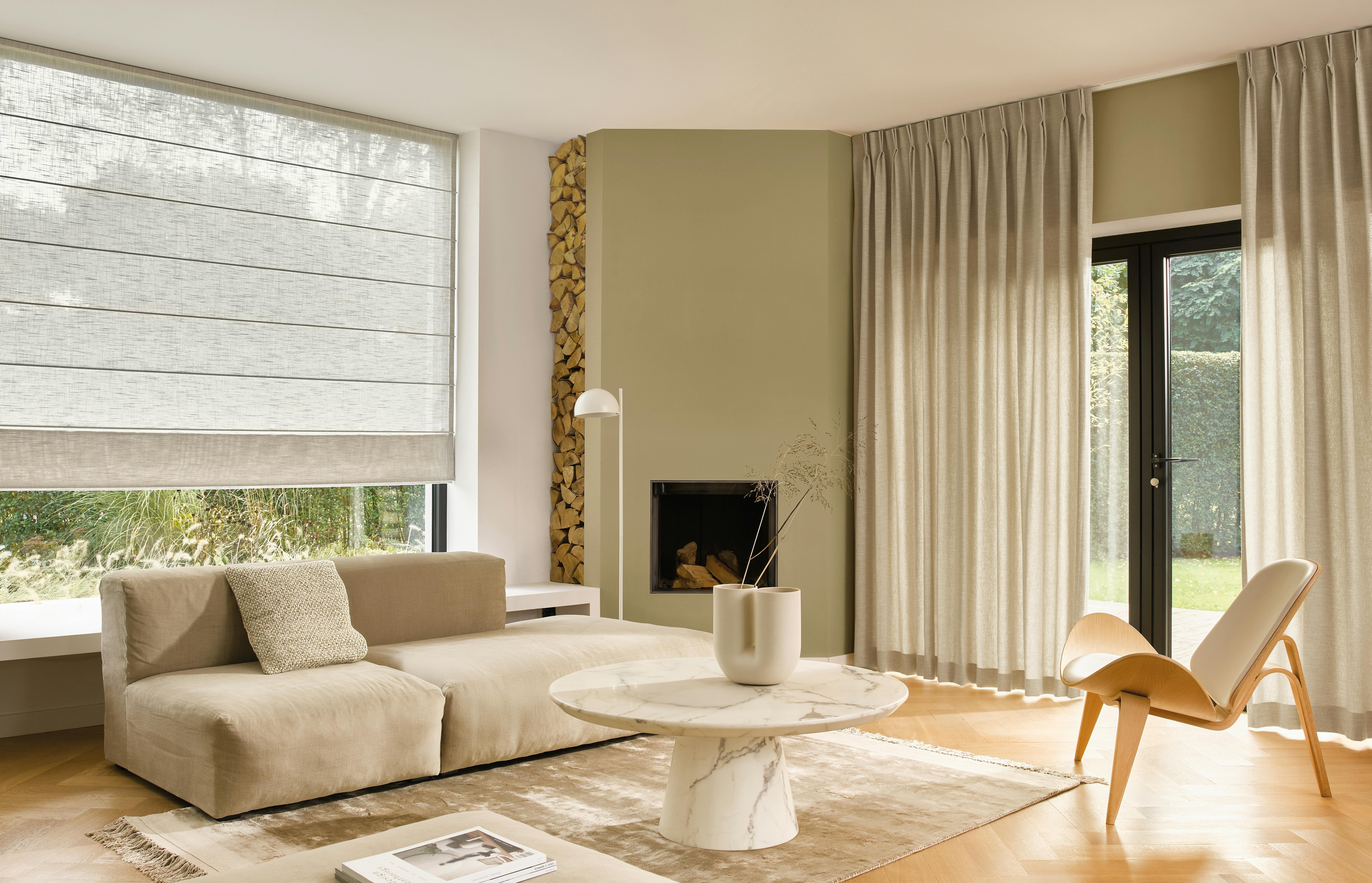 Crèmekleurige gordijnen op de terrasdeur en witte vouwgordijnen op een groot raam in een ruime woonkamer