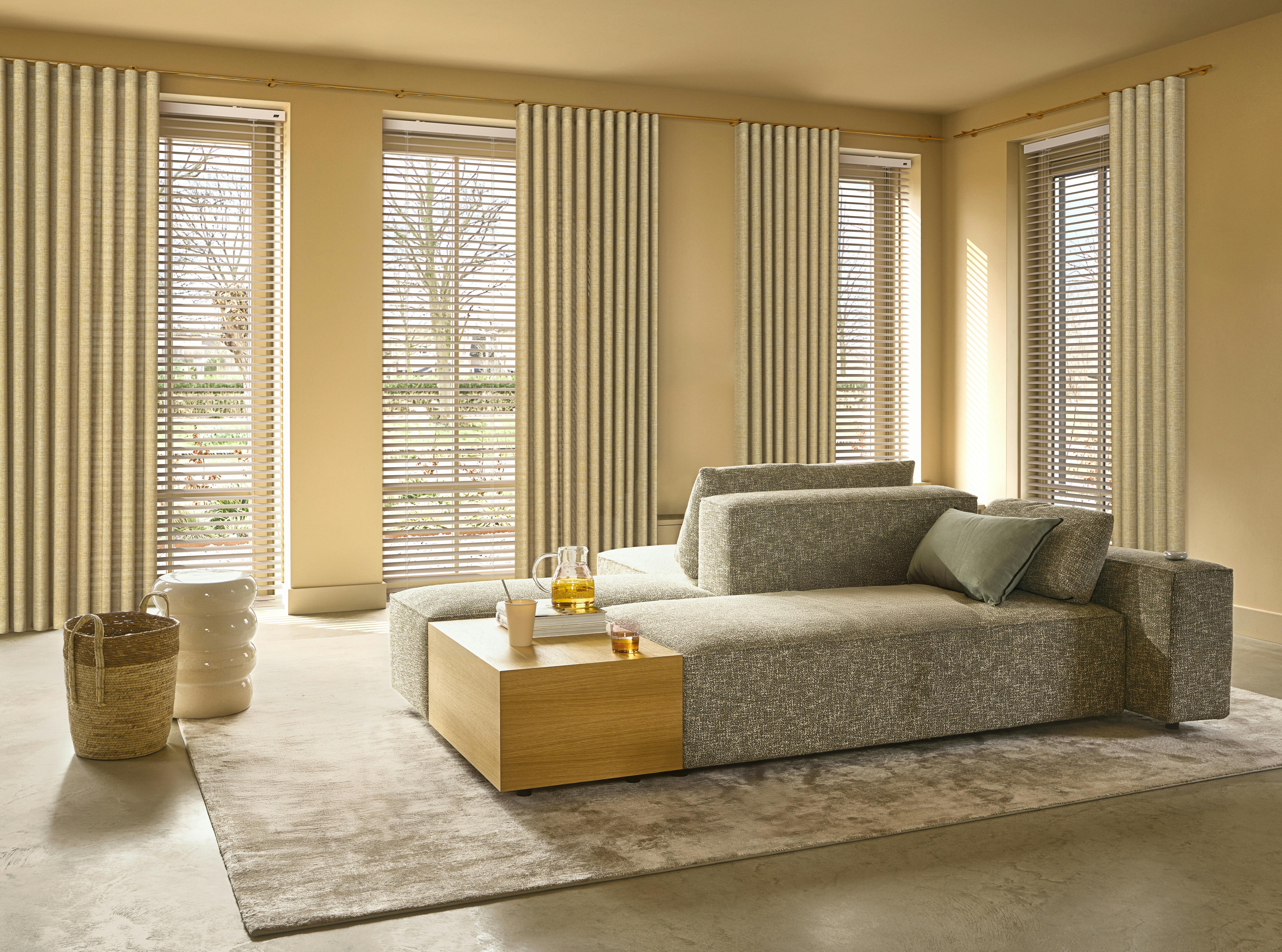 Crèmekleurige gordijnen en jaloezieën voor ramen in een lichte, gele woonkamer