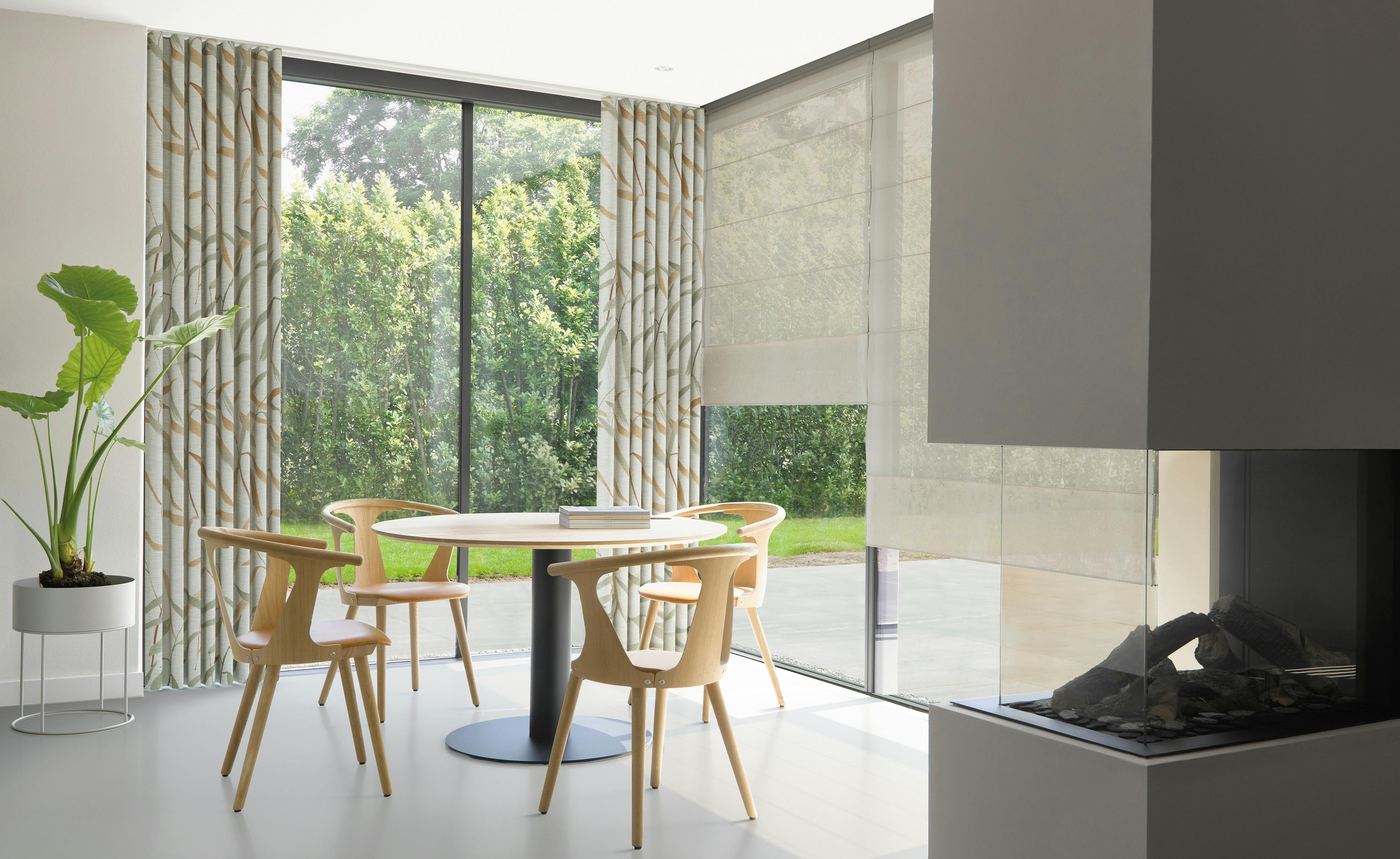 Cream roman blinds and light patterned curtains on large windows in a cosy dining room 