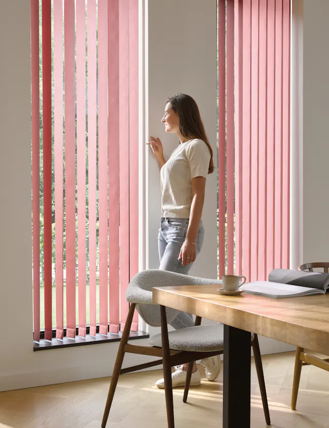 Kvinne ved et vindu med røde lamellgardiner i en spisestue