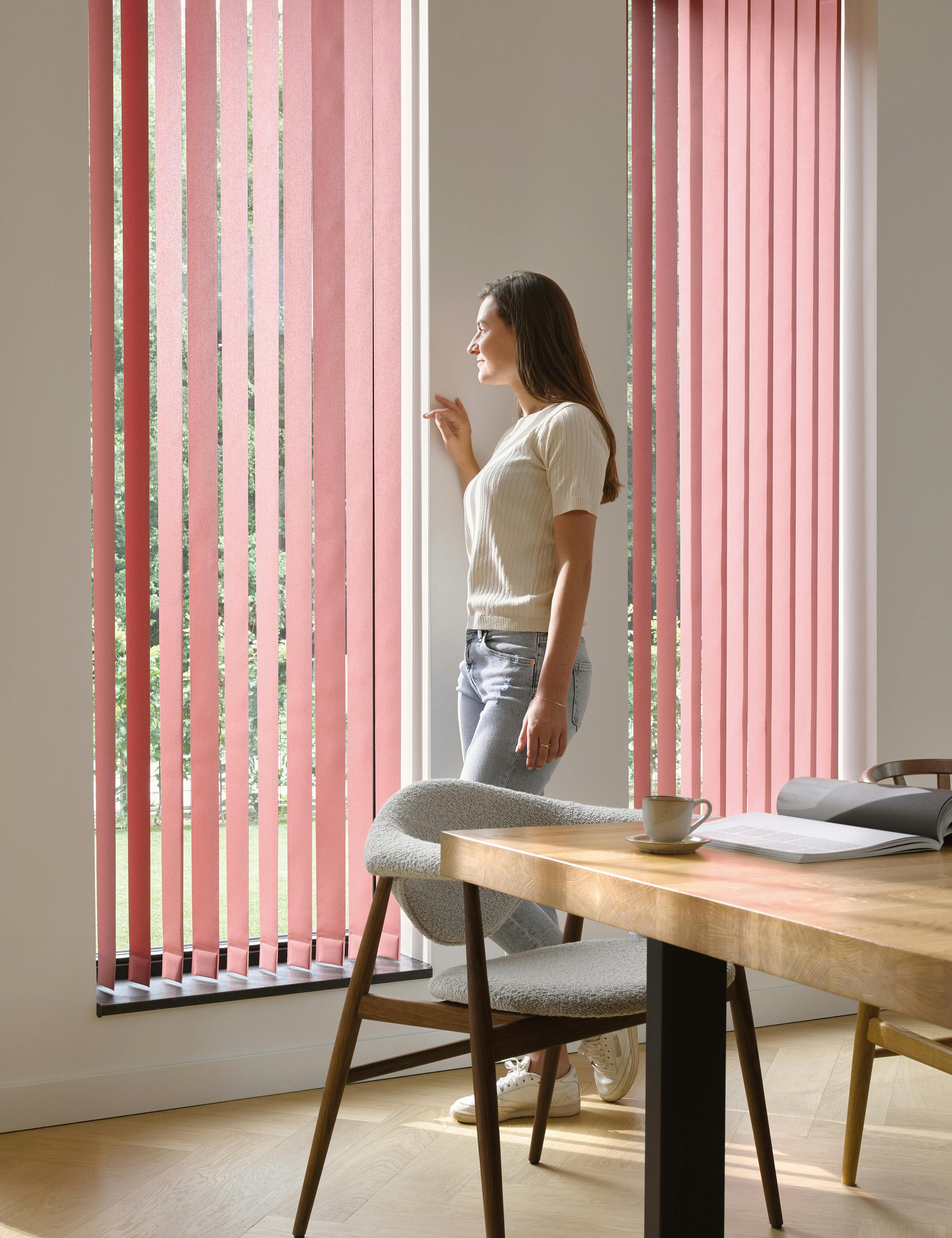 En kvinne ved et vindu med røde lamellgardiner i spisestuen