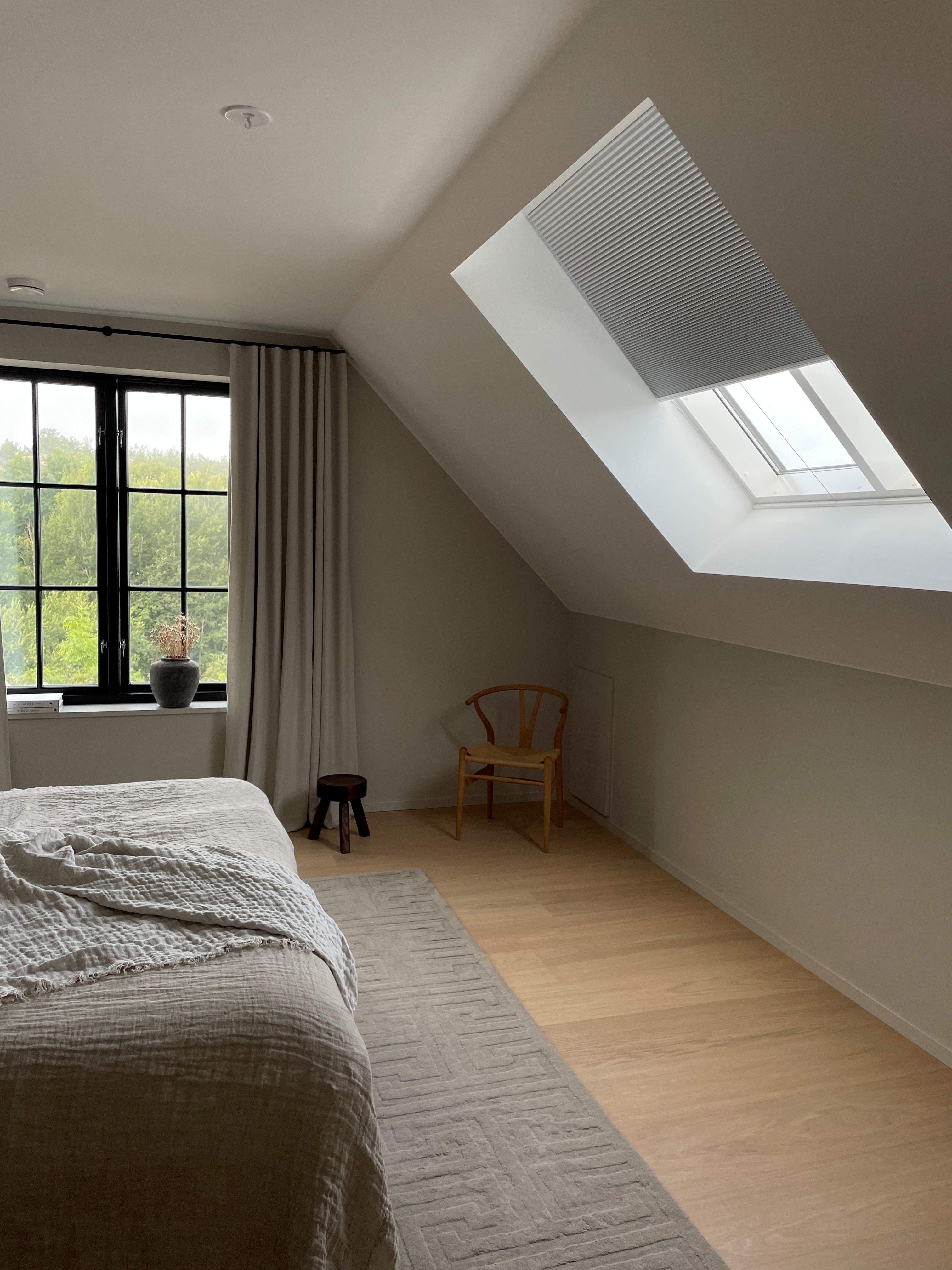 Grey duette shades on a skylight window and beige curtains in a bedroom 