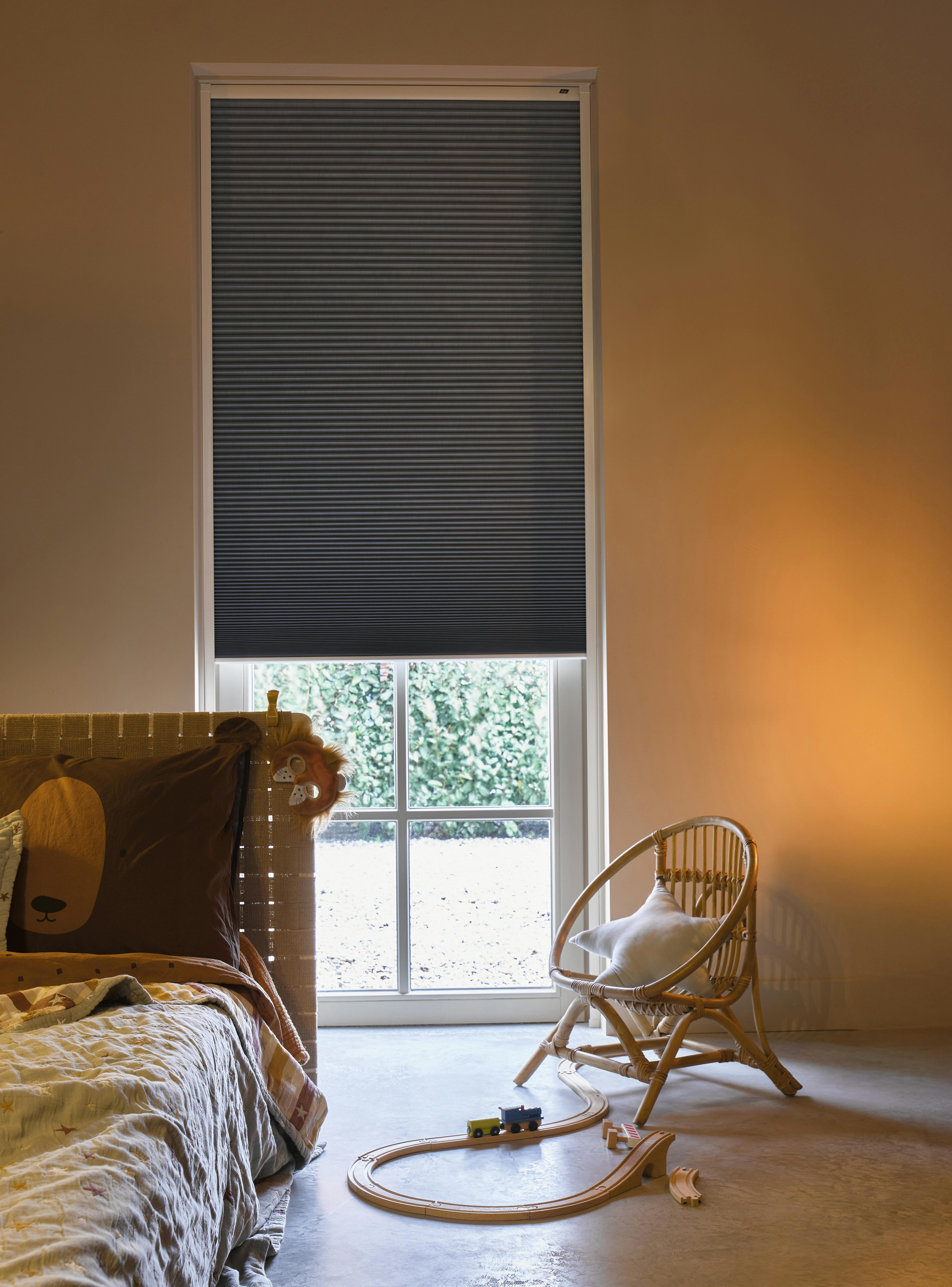 Donkergrijze verduisterende Duette® shades op een raam in een kinderkamer