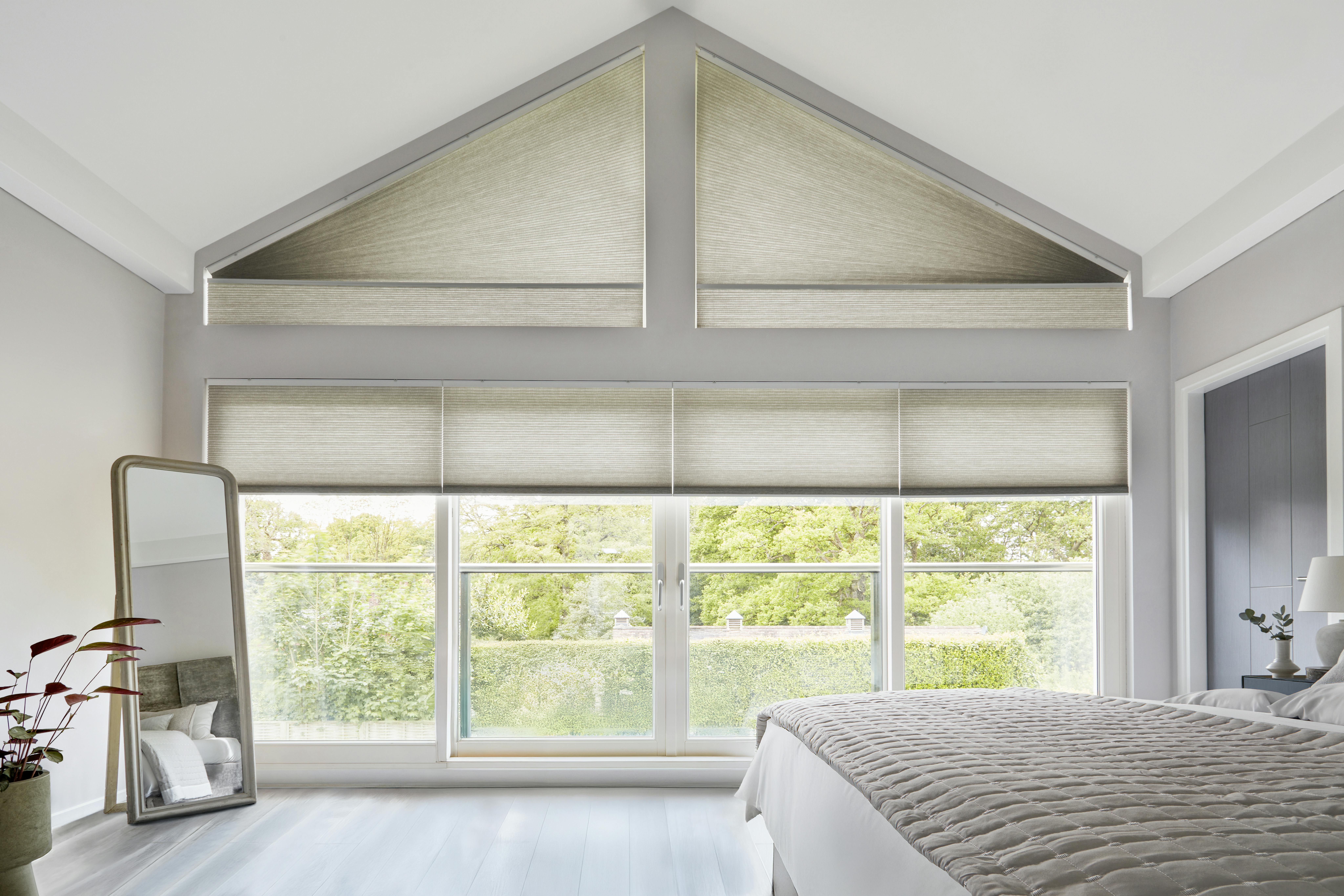 Crèmekleurige Duette® shades op grote ramen en een puntgevelraam in de woonkamer