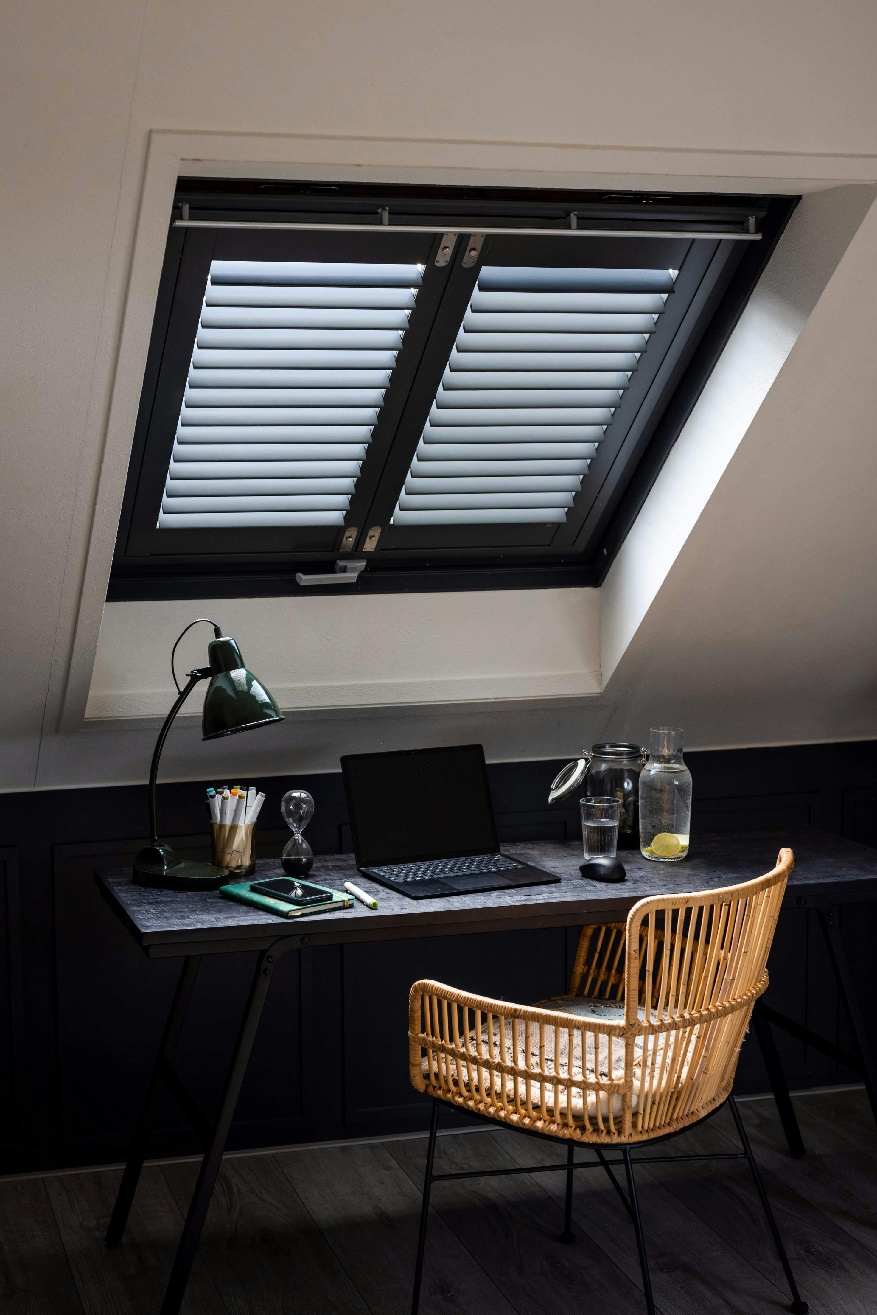 Zwarte shutters op een dakraam in een thuiskantoor