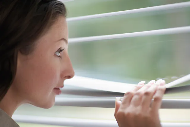 Nærbilde av aluminiumspersienner med en kvinne som titter gjennom