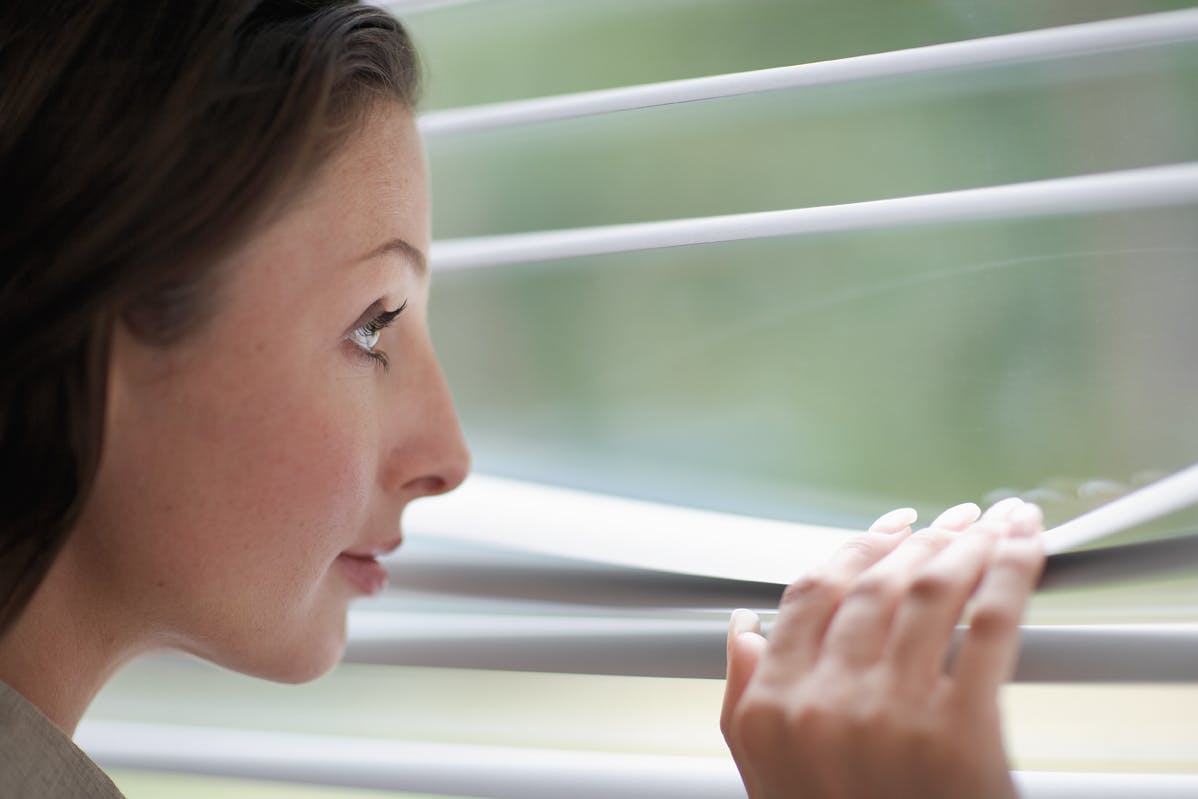 Gros plan sur des stores vénitiens en aluminium avec une femme qui regarde à travers
