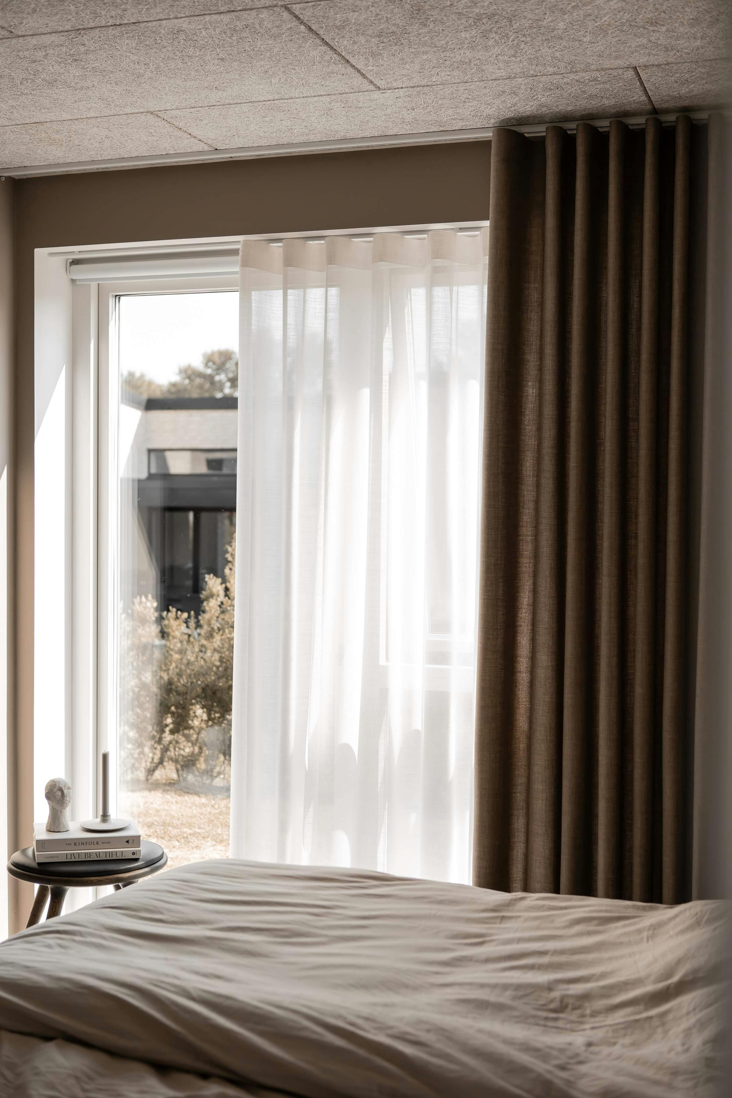 Brown curtains layered over sheer curtains covering large bedroom windows