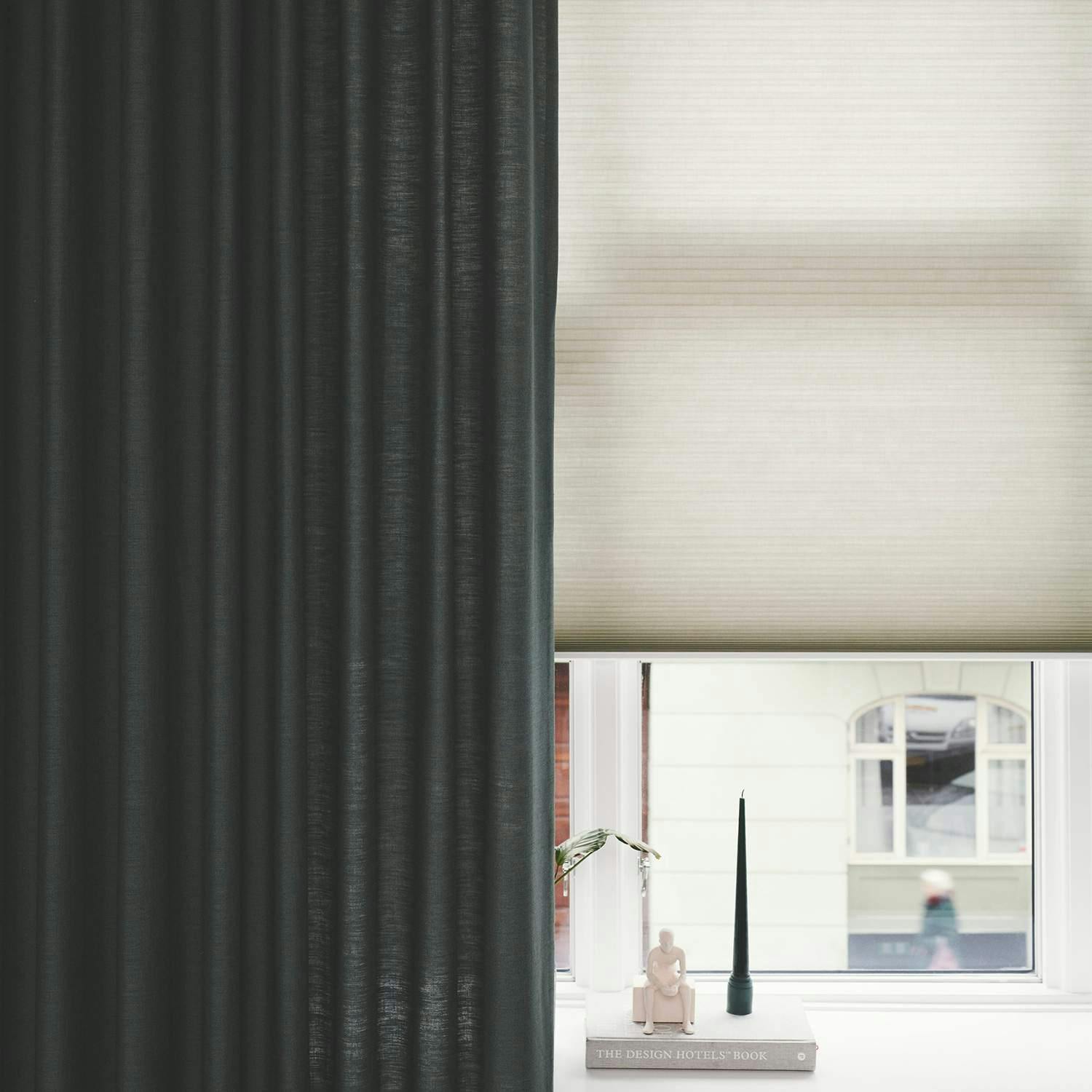 Close up of green curtain layered over cream pleated blind