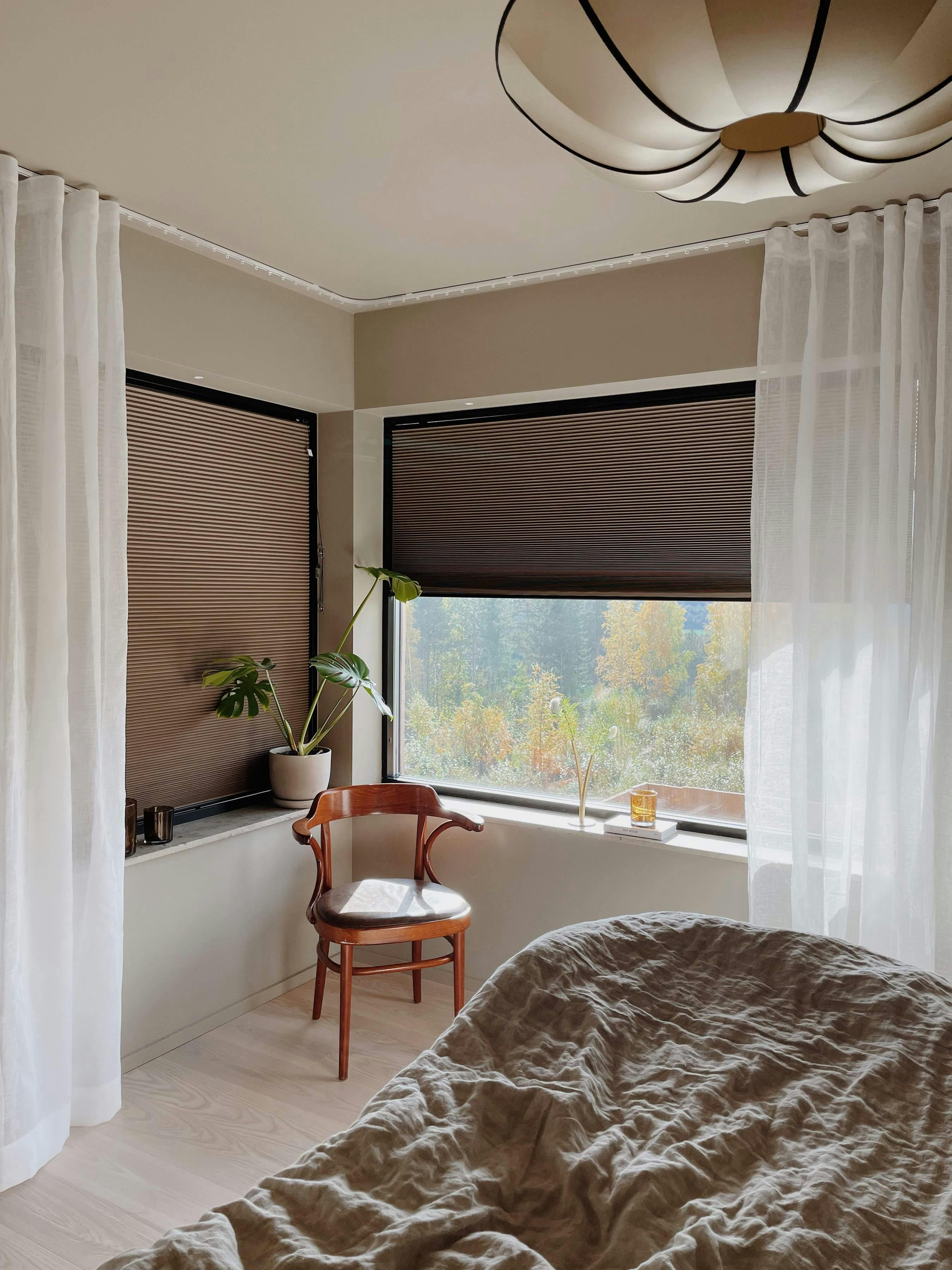 Brown duette blinds and white sheer curtains partially covering bedroom windows