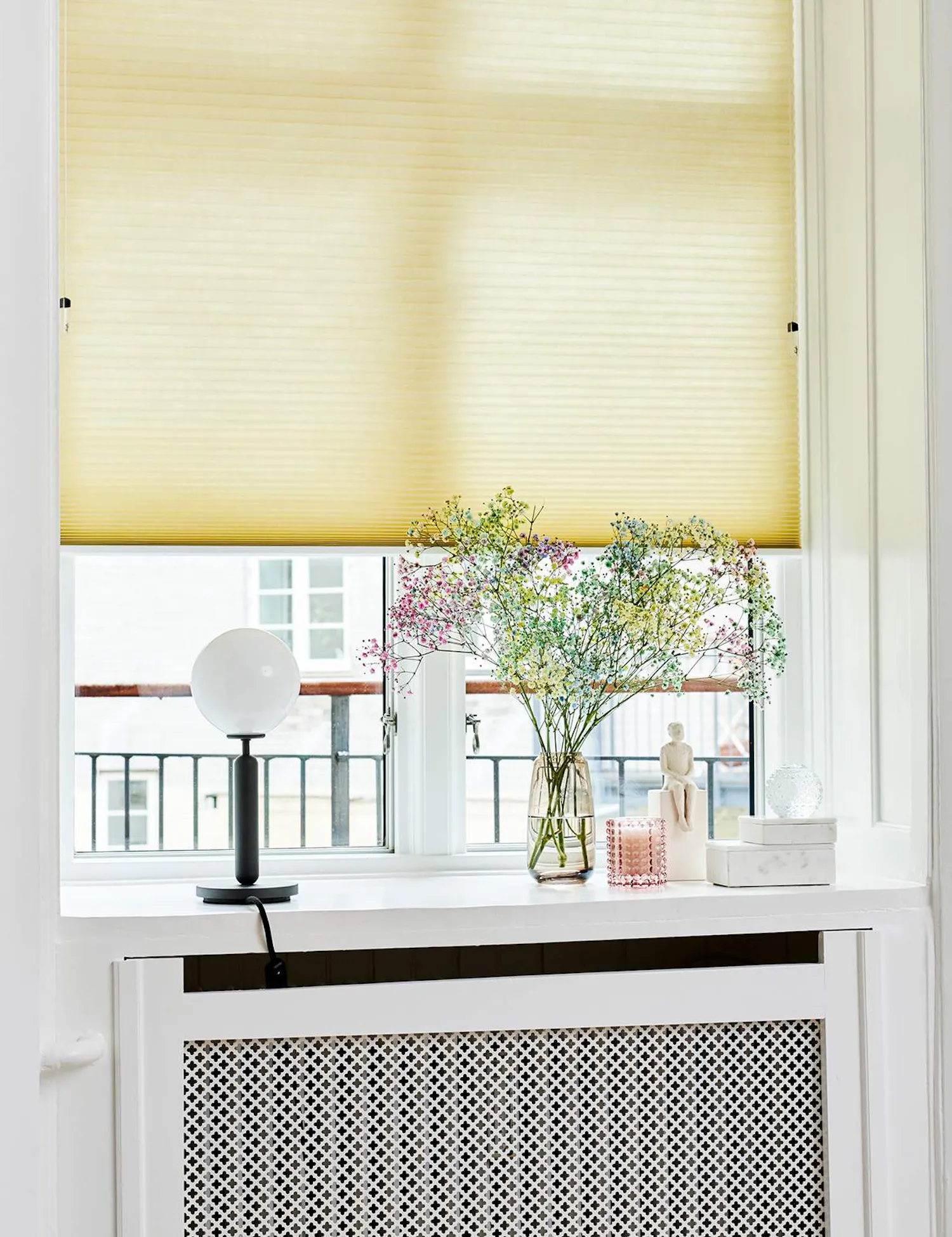 Yellow pleated blind covering tall thin window in a white setting