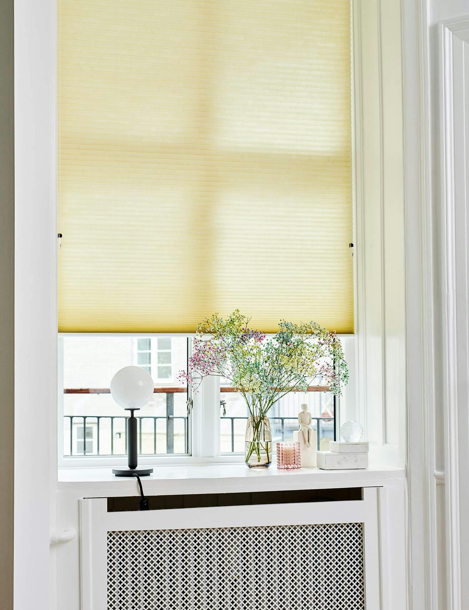 Yellow pleated blind covering tall thin window in a white setting