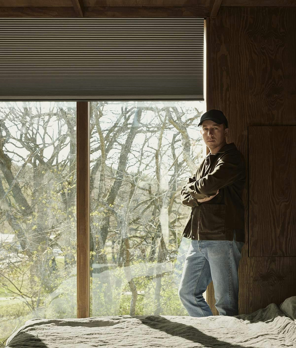 Andreas Martin posing in front of large windows in front of his garden