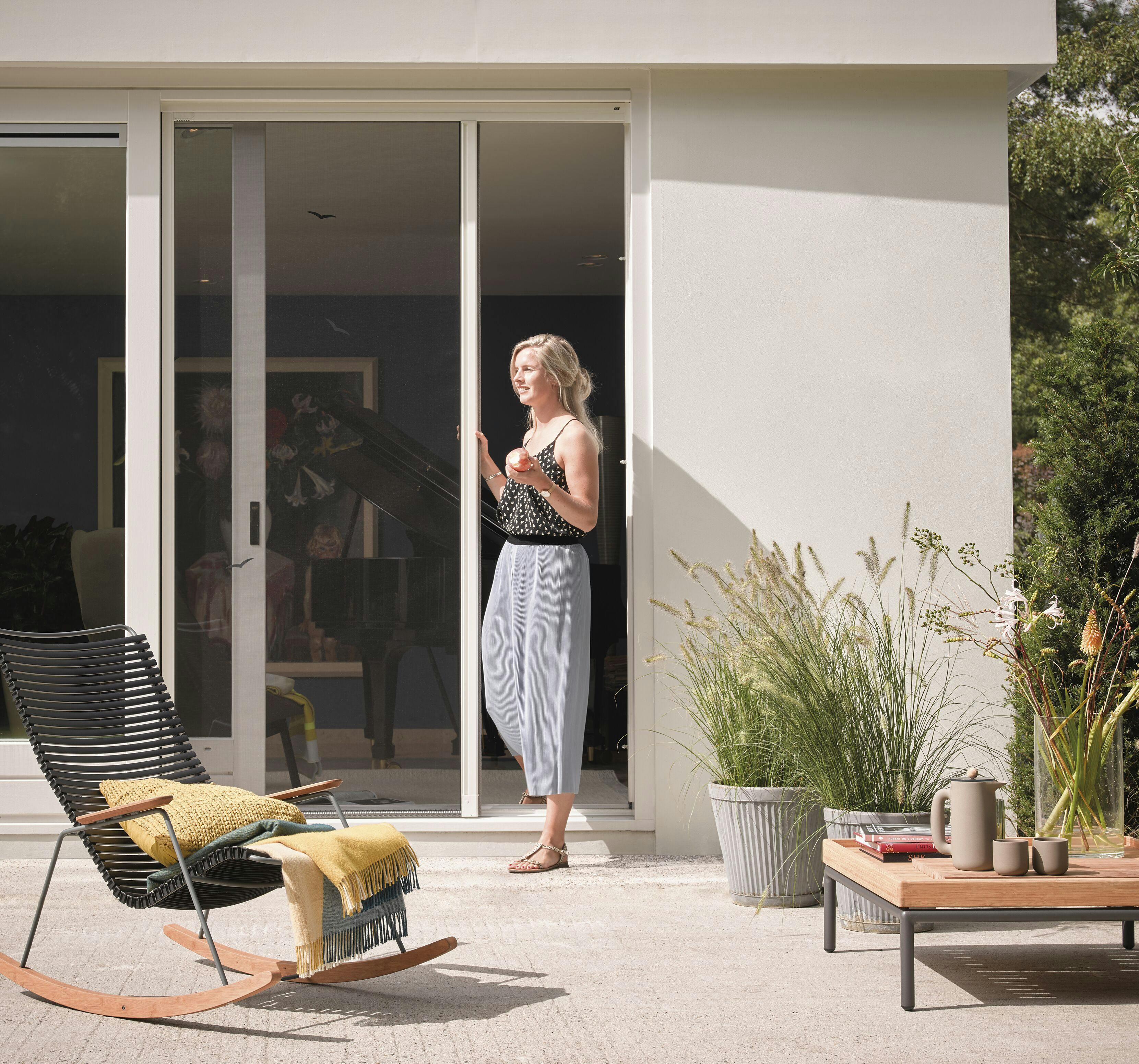 Een vrouw die een rolhordeur opent in een lichte achtertuin