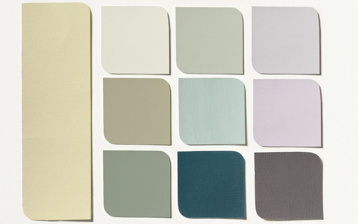 En samling färgprover ordnade i ett rutmönster med nio mindre och en större färgruta till vänster. Färgerna sträcker sig från ljusa till mörka nyanser, inklusive kräm, beige, ljusgrå, mintgrön, teal, lavendel och mörkgrå. Proverna har rundade hörn upptill till höger.