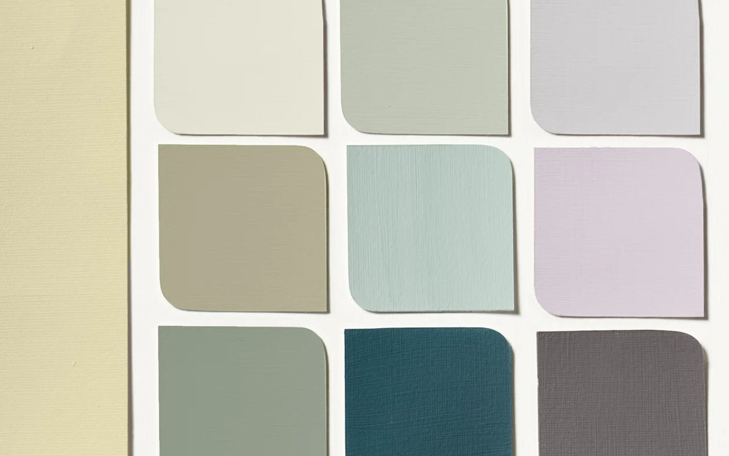 En samling färgprover ordnade i ett rutmönster med nio mindre och en större färgruta till vänster. Färgerna sträcker sig från ljusa till mörka nyanser, inklusive kräm, beige, ljusgrå, mintgrön, teal, lavendel och mörkgrå. Proverna har rundade hörn upptill till höger.