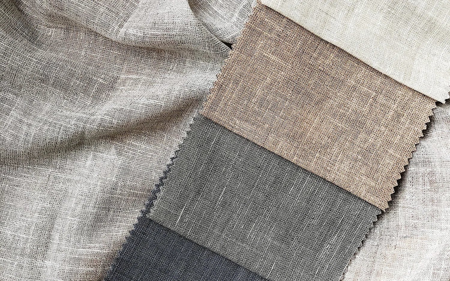 En stapel med tygprover i neutrala färger som beige, brunt och grått, med grov textur. Proverna ligger ovanpå ett större tygstycke med liknande mönster.